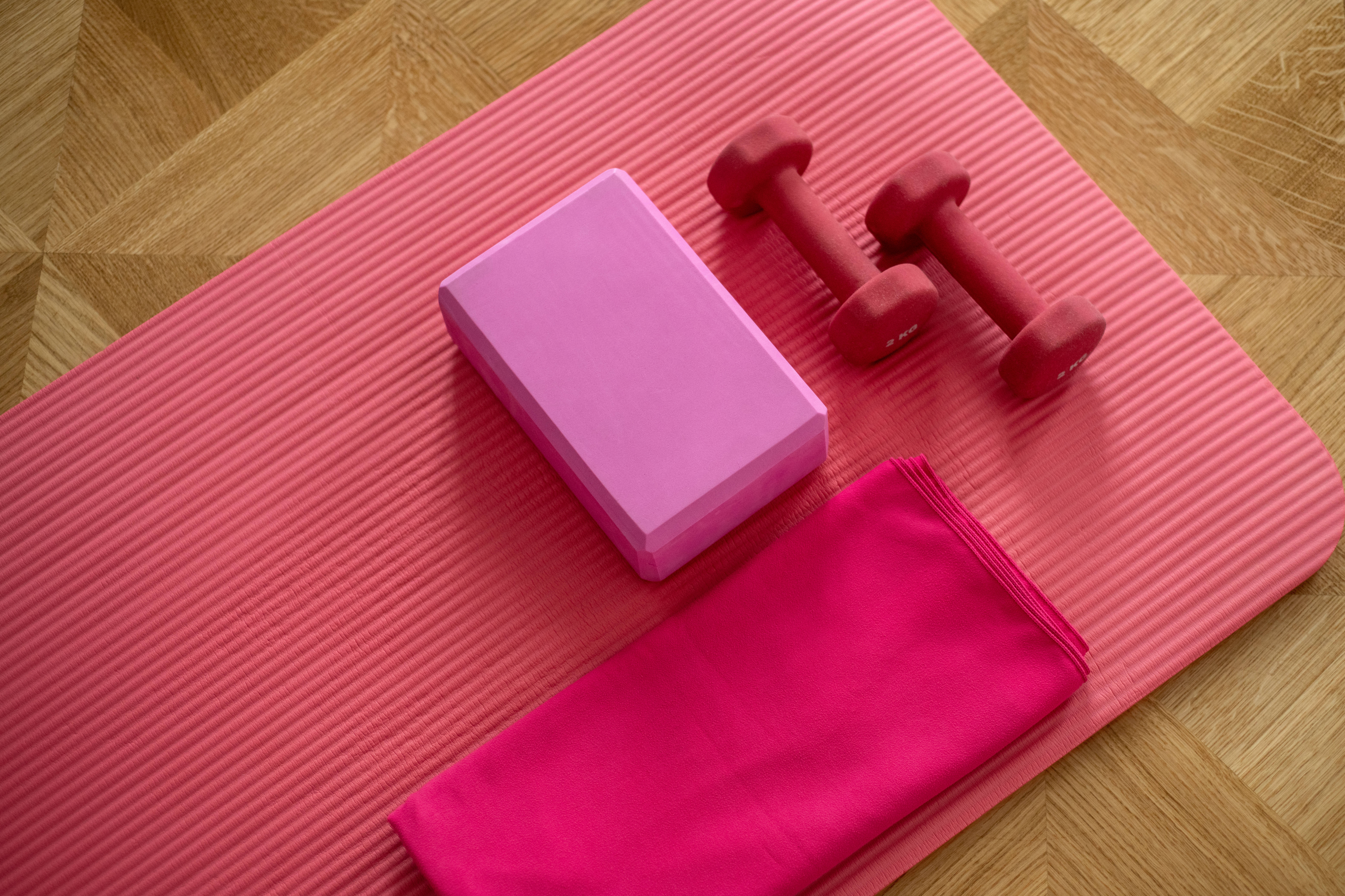Exercise 桌布 壁紙 — 粉紅色瑜伽墊上放有粉紅色瑜伽磚、紅色啞鈴和亮粉紅色毛巾，排列在木地板上。