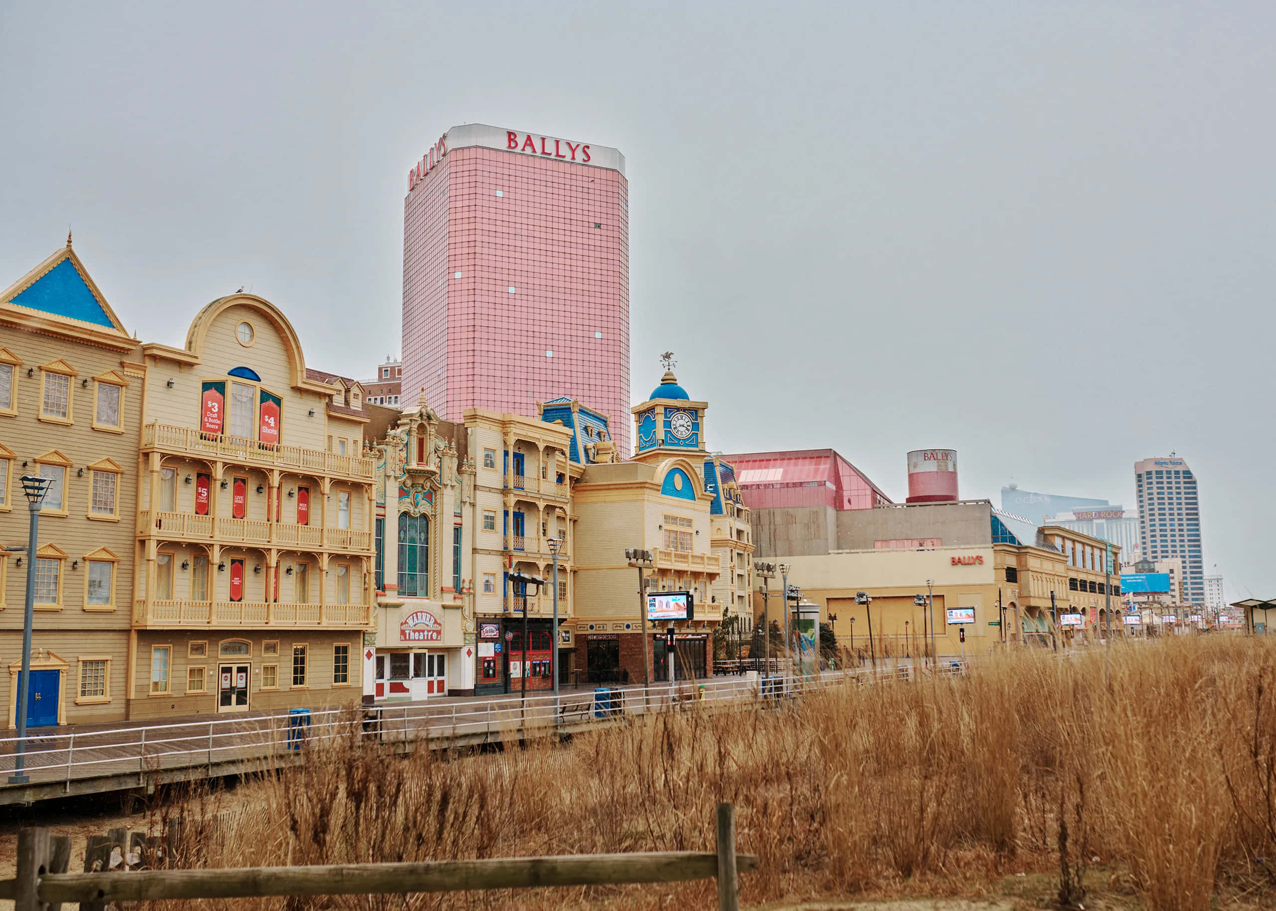 Buildings 桌布 壁紙 — 粉紅色的Bally's賭場塔樓在華麗的黃色建築後面升起，沿著水邊，前景有乾燥的蘆葦。
