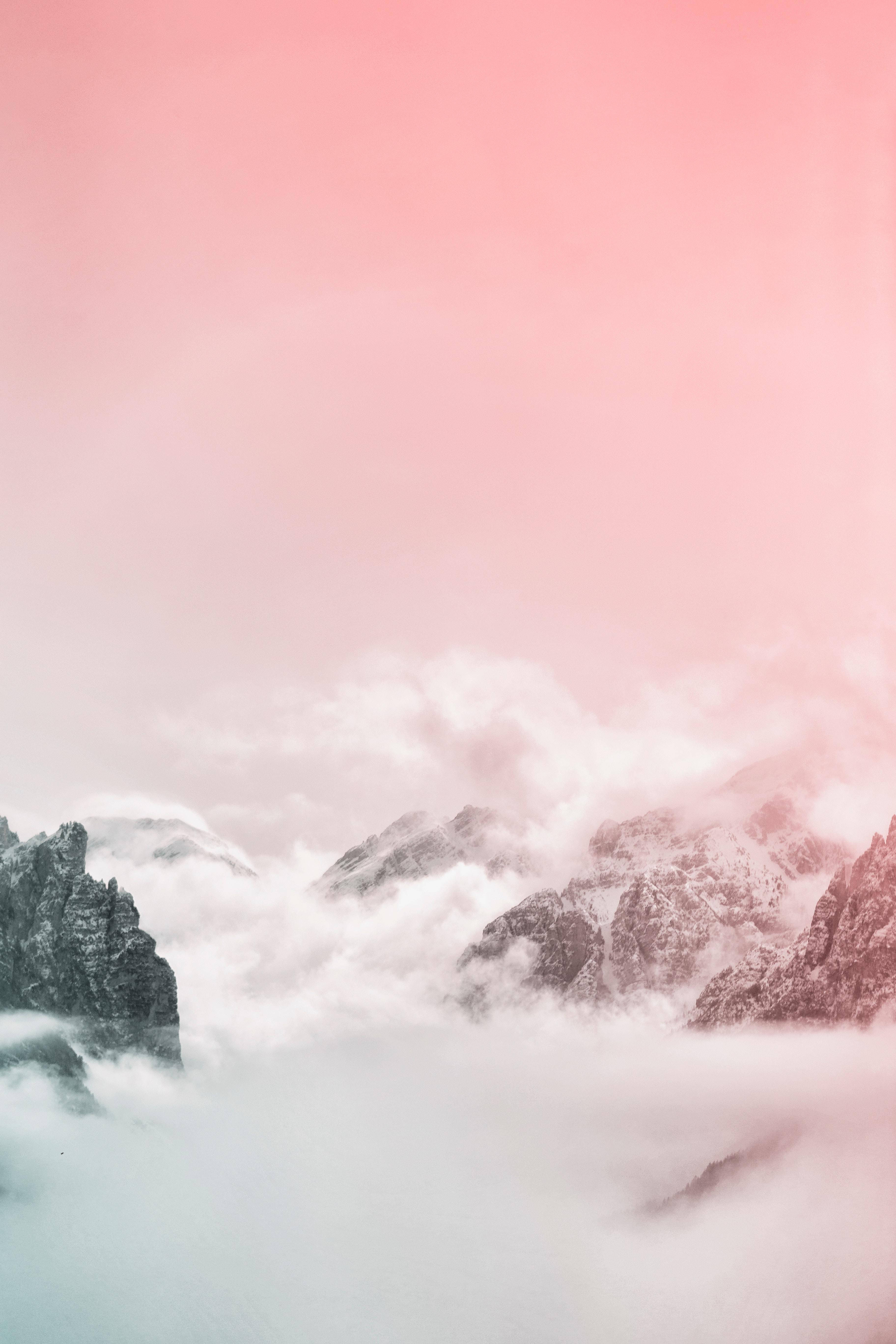 Pastel iPhone 桌布 壁紙 — 粉紅色的天空和雲朵飄過從霧谷中浮現的積雪山峰。