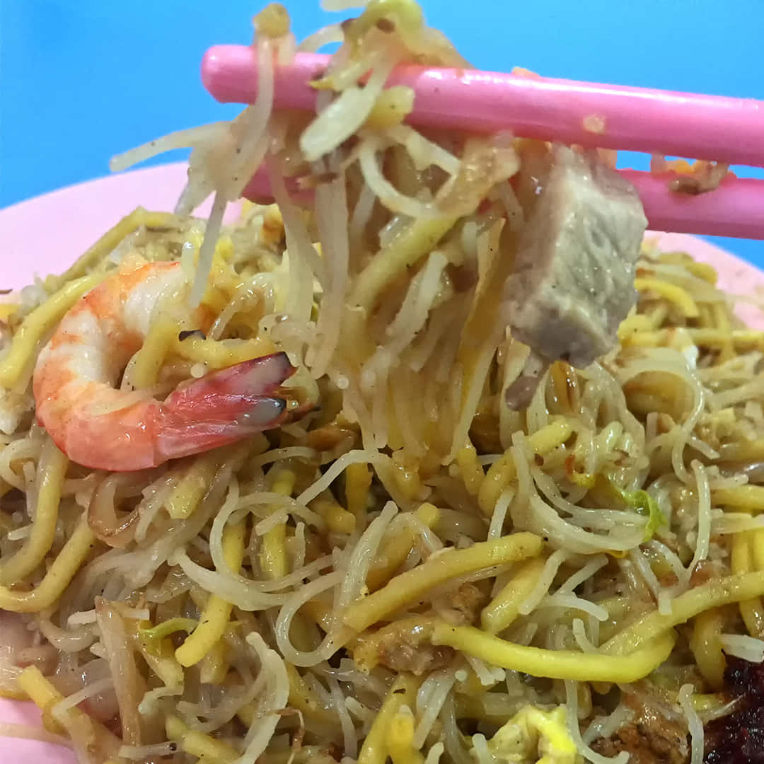 Noodles 桌布 壁紙 — 粉紅色筷子從粉紅色盤子上夾起帶有蝦子和豆芽的亮黃色米粉，背景為亮藍色。