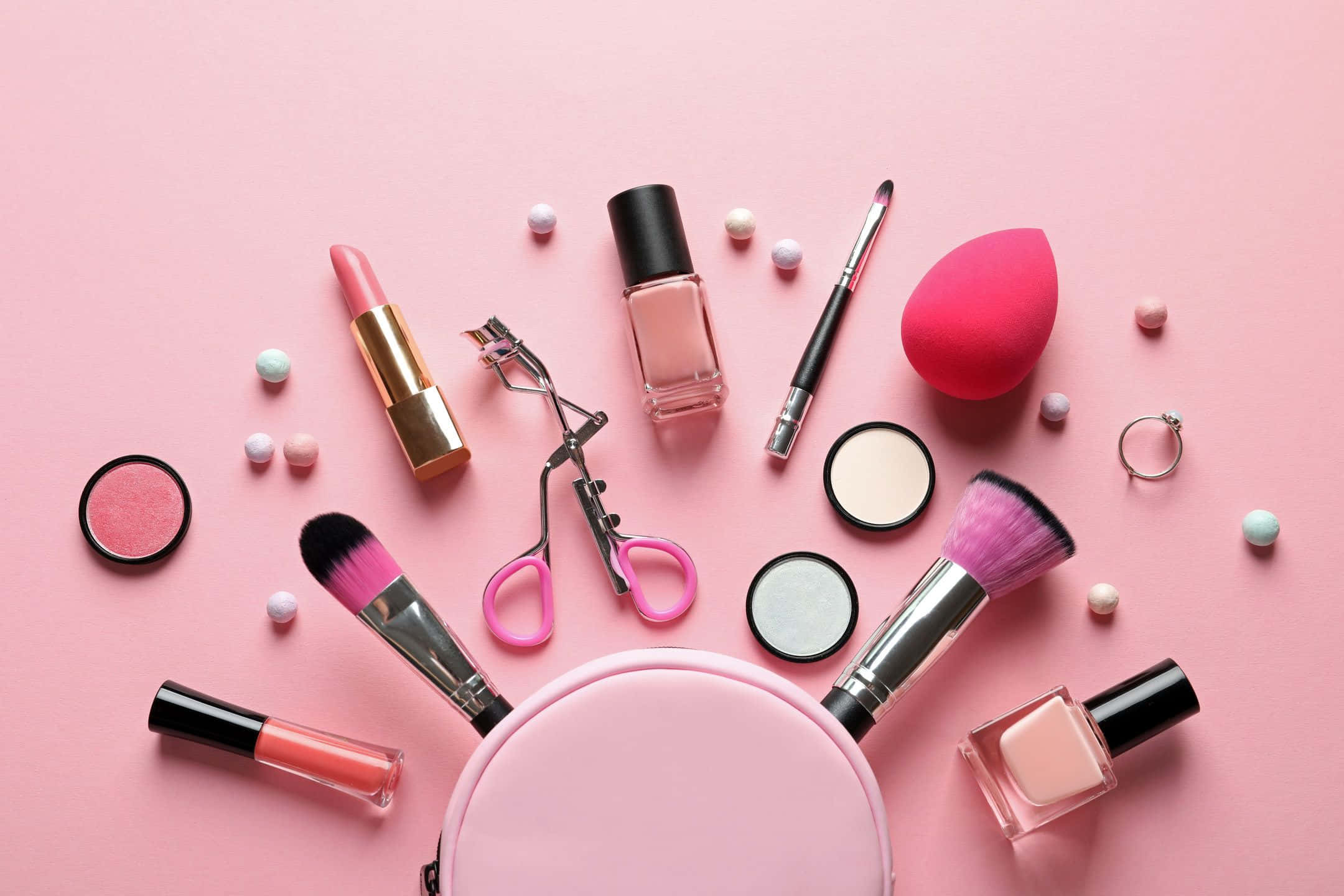 Pink Makeup 桌布 壁紙 — 粉紅色美容產品的平鋪擺設，包括唇膏、指甲油、刷子和化妝海綿，散落在柔和的粉紅色背景上。