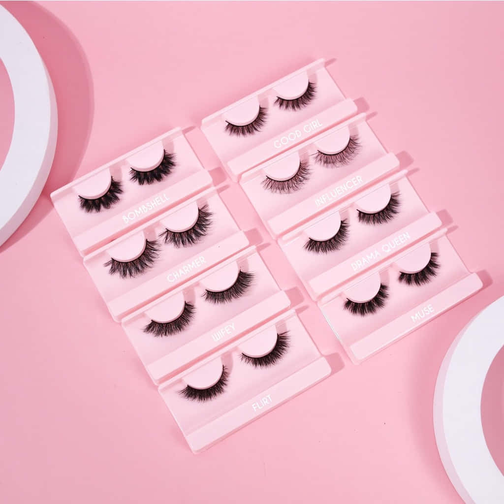 Eyelash 桌布 壁紙 — 粉紅色背景展示八對假睫毛，放在透明盒中，標有俏皮風格如「Good Girl」和「Drama Queen」。