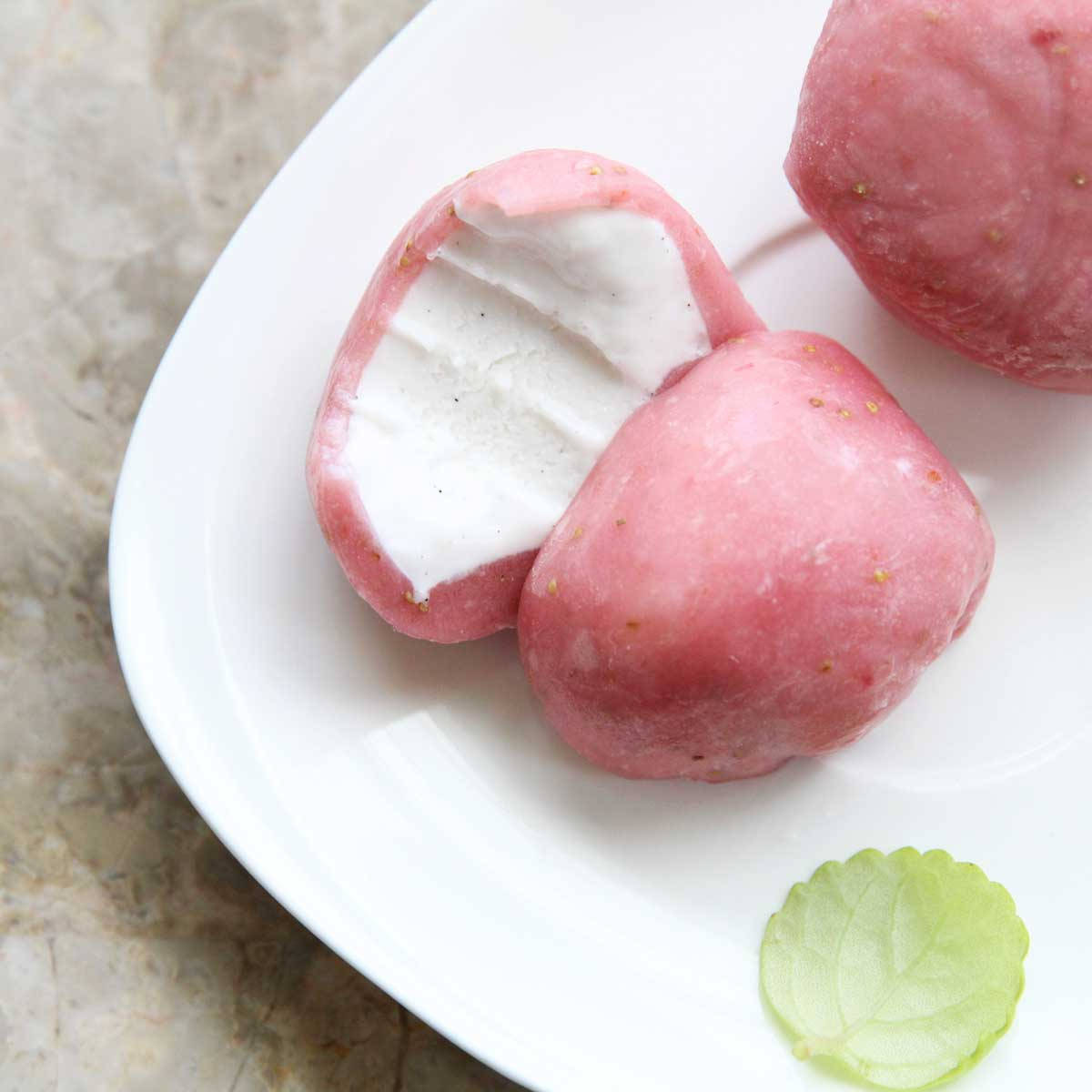 Mochi 桌布 壁紙 — 粉紅色草莓味麻糬搭配白色奶油餡料，放在白色盤子上，旁邊有一片綠葉。