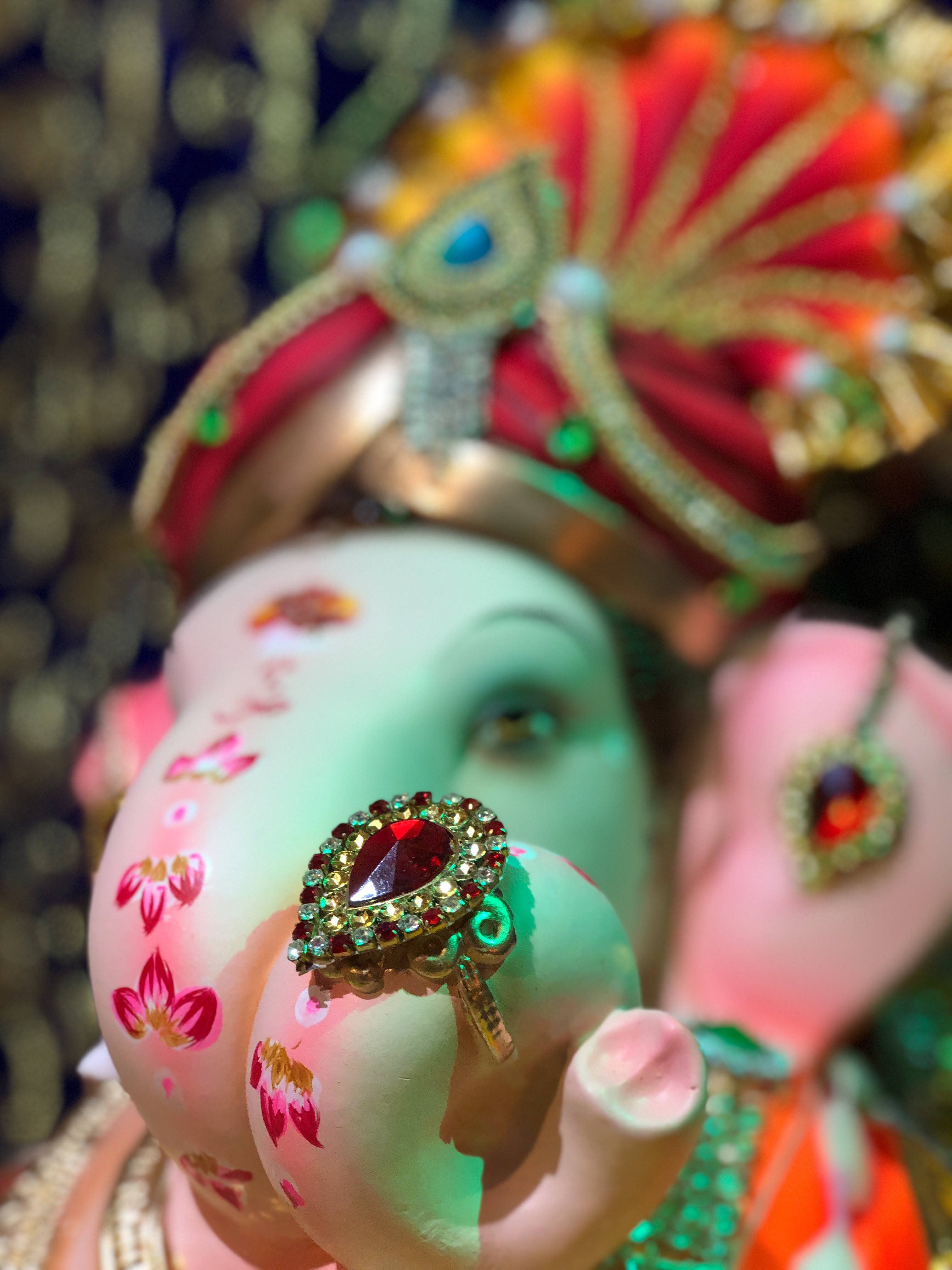 Bappa 桌布 壁紙 — 粉紅色象頭神雕像特寫，飾有花卉圖案和象鼻上的寶石戒指，背景是閃閃發光的金色。
