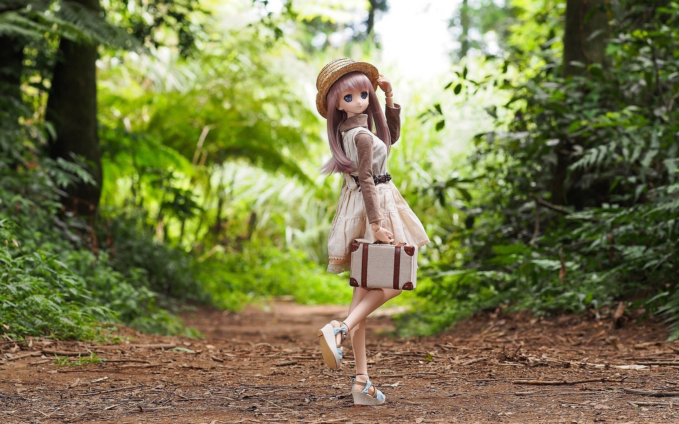 Doll 桌布 壁紙 — 粉紅色頭髮、戴草帽的動漫風格娃娃，沿著陽光斑駁的森林小徑行走，手提復古行李箱。