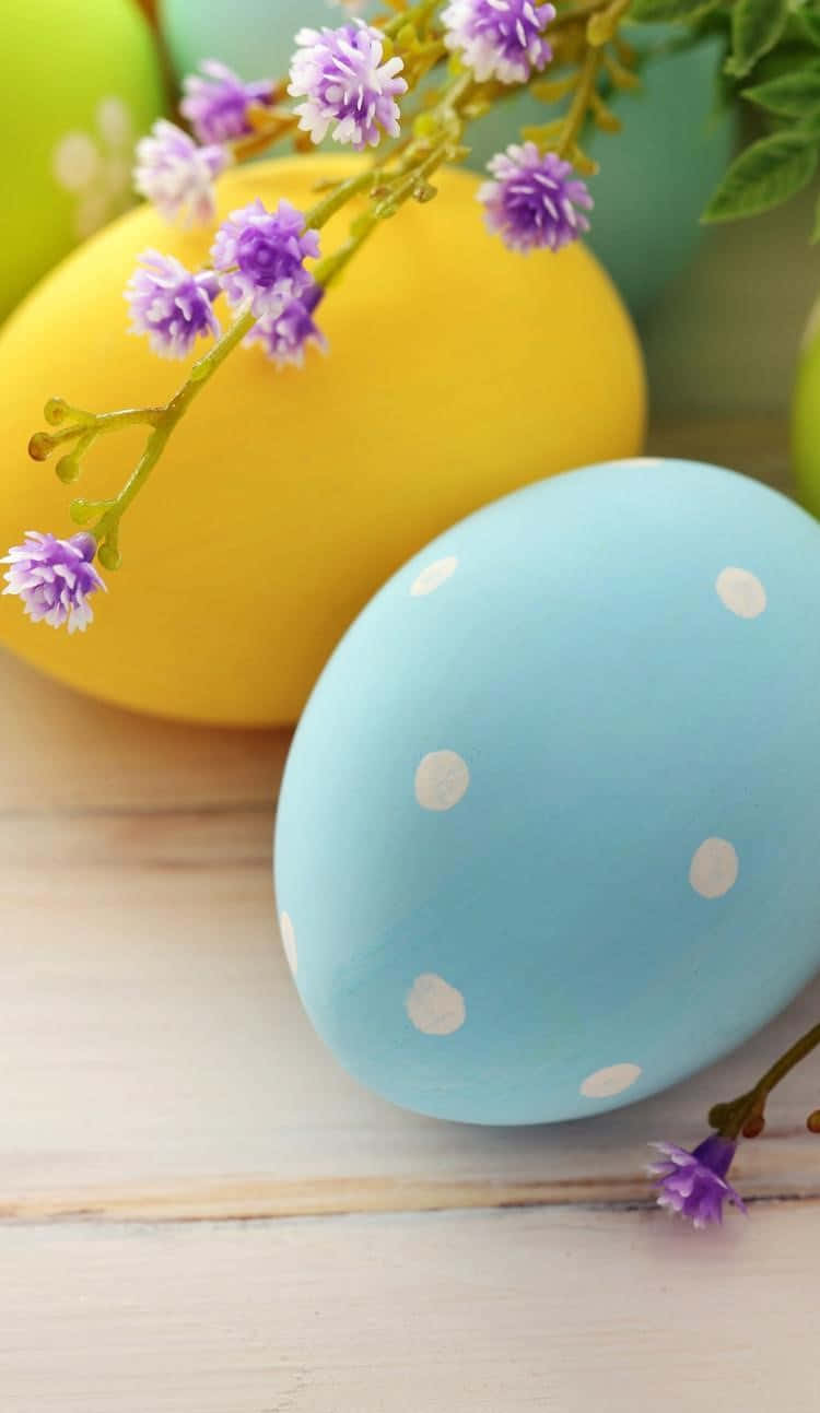 Cute Easter iPhone 桌布 壁紙 — 粉藍色和黃色的復活蛋帶有白色圓點，放在木質表面上，旁邊有精緻的紫色花朵。