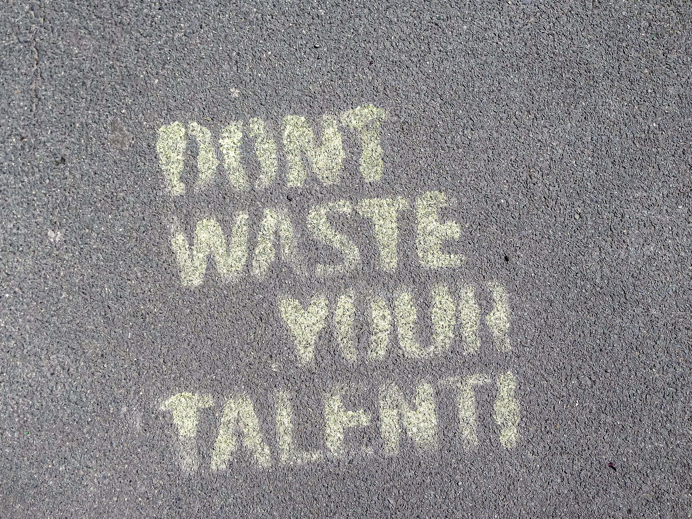 personal 桌布 壁紙 — 粗獷的塗鴉訊息「DON'T WASTE YOUR TALENT!」以褪色白色噴漆在粗糙的瀝青路面上。