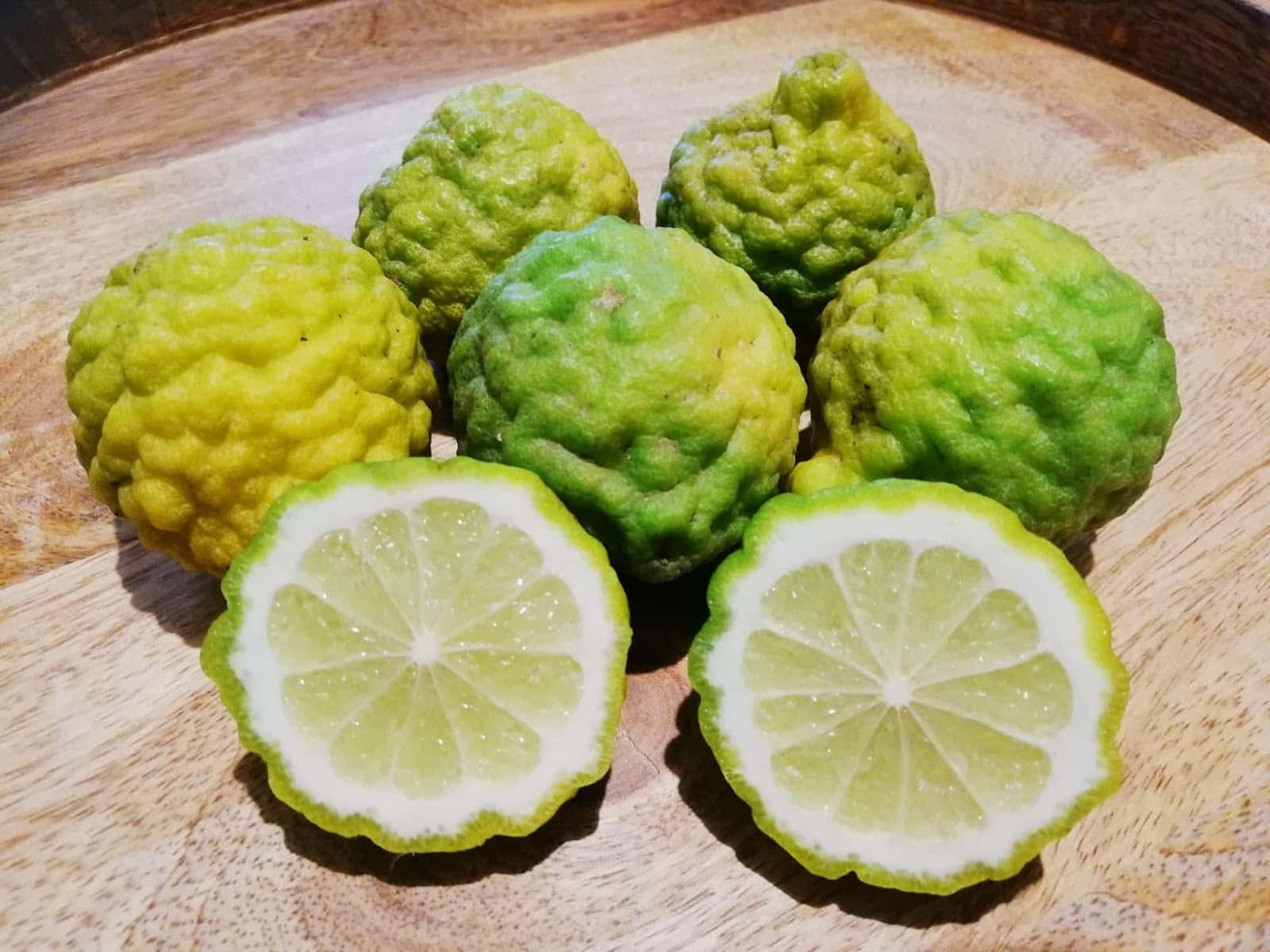 Fruit 桌布 壁紙 — 粗糙外皮的泰國青檸和兩個切半的檸檬放在溫暖的木板上，展現出鮮豔的綠色色調和多汁的果肉。