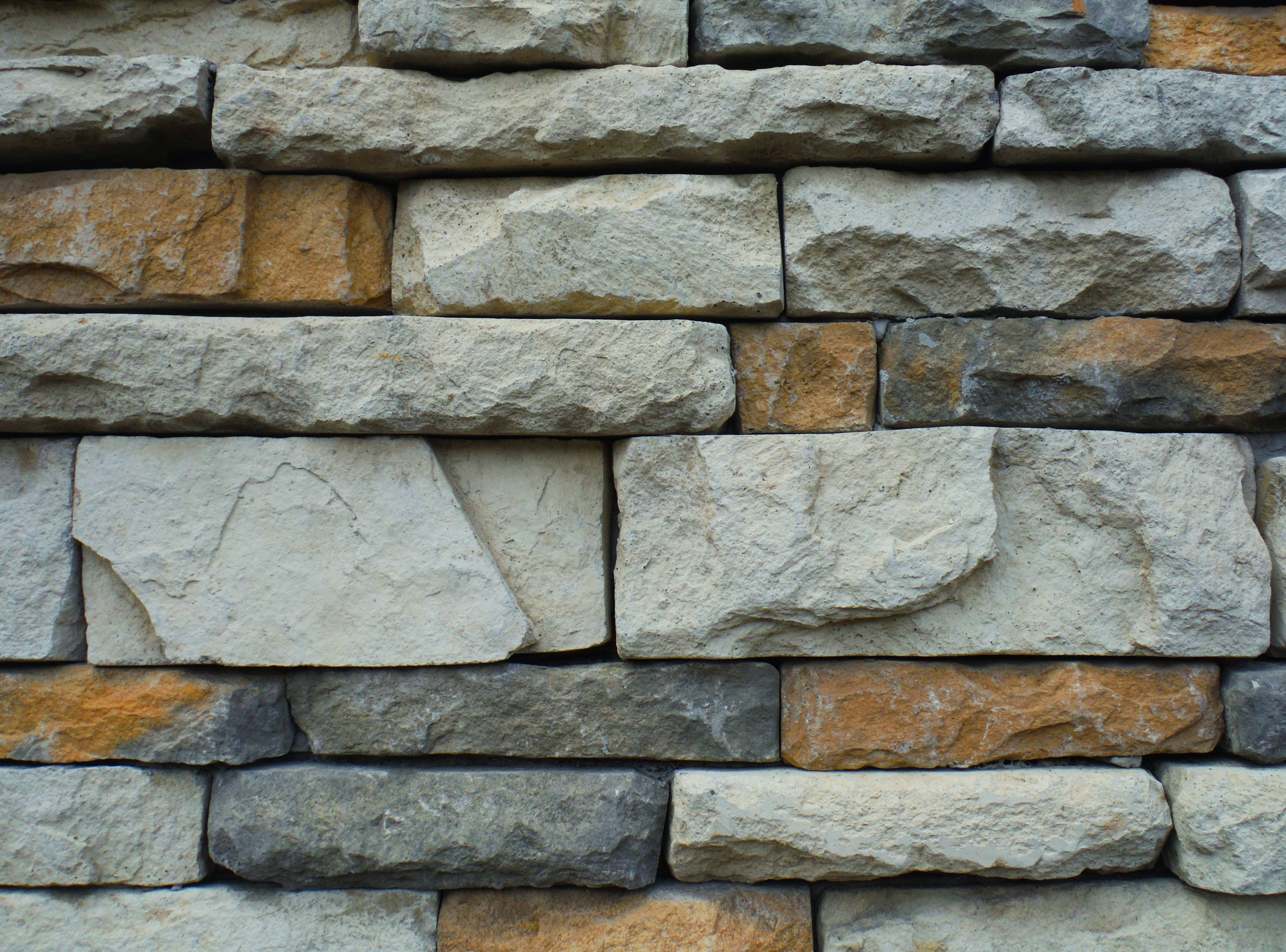 Stone Wall 桌布 壁紙 — 粗糙石牆的特寫，帶有各種灰色、米色和橙色色調以及粗糙紋理的塊狀結構。