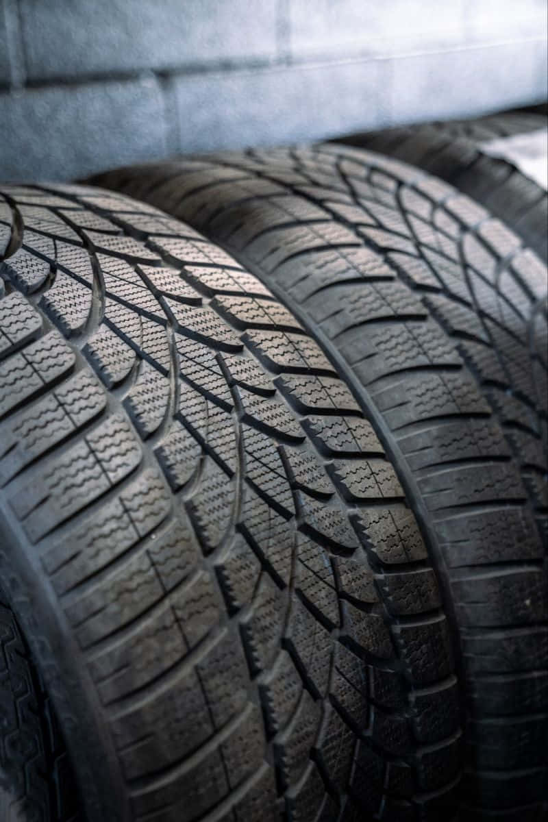 Winter Tires 桌布 壁紙 — 粗糙黑色冬季輪胎胎面特寫，背景為模糊的灰色混凝土牆。