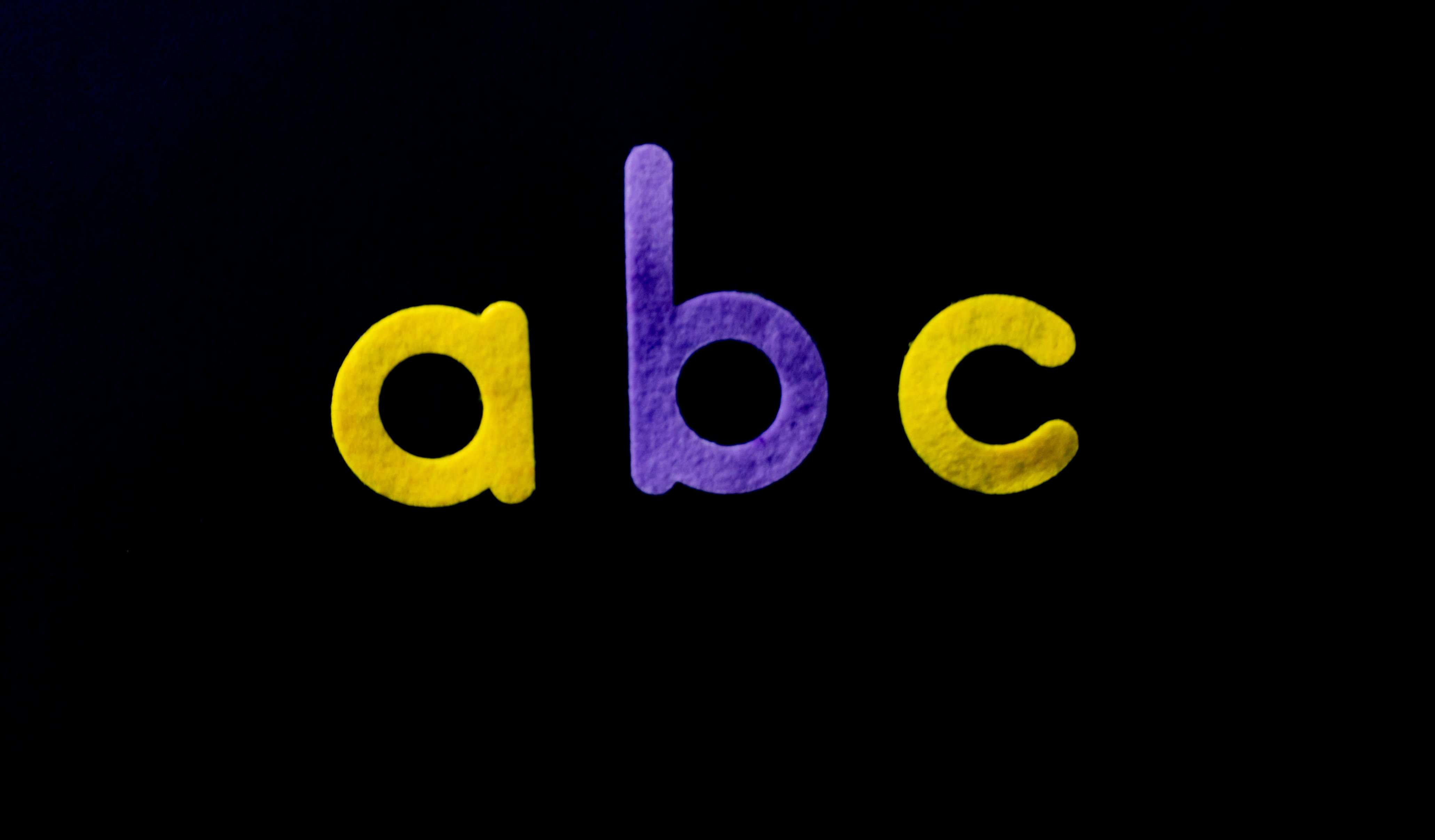 abc 桌布 壁紙 — 粗體小寫字母 abc 在深黑色背景上發出紋理黃色和紫色的光芒。