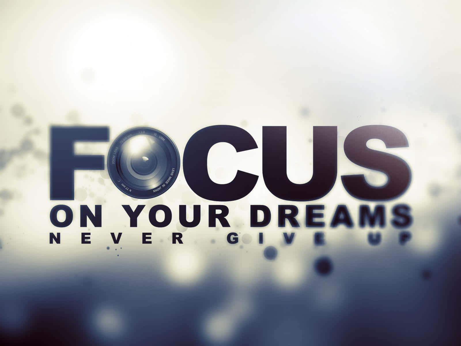 Focus 桌布 壁紙 — 粗體文字寫著專注於你的夢想永不放棄，相機鏡頭取代了字母O，背景柔和模糊。