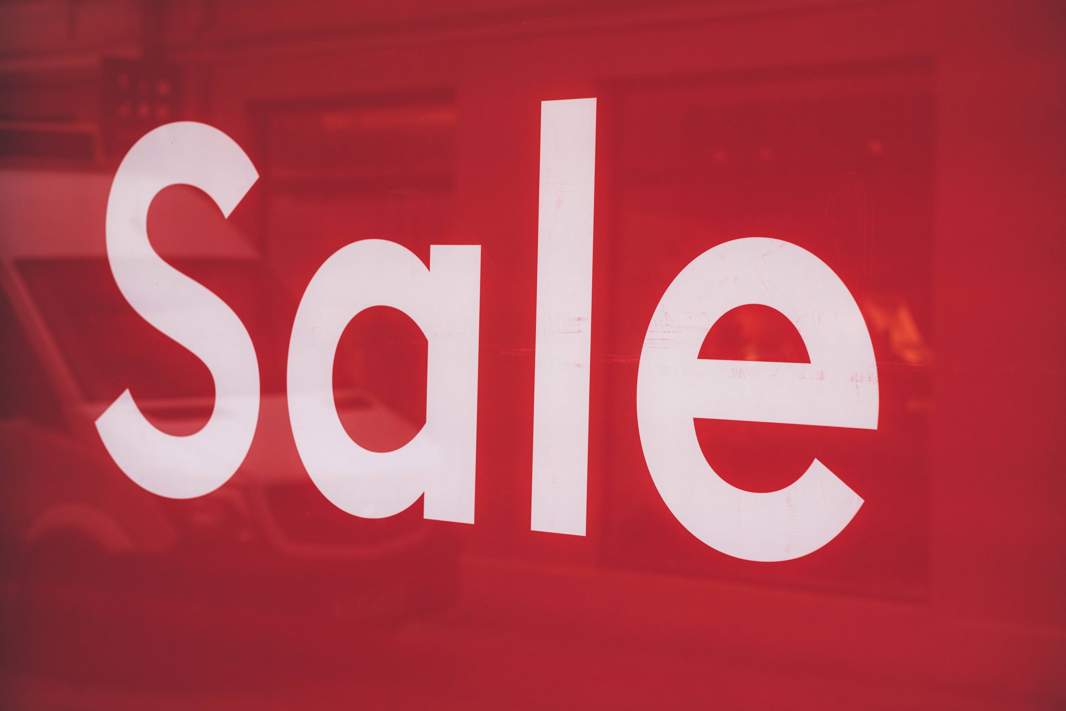 Sales 桌布 壁紙 — 粗體白色「Sale」文字在充滿活力的紅色玻璃店面中脫穎而出，並帶有模糊的城市倒影。