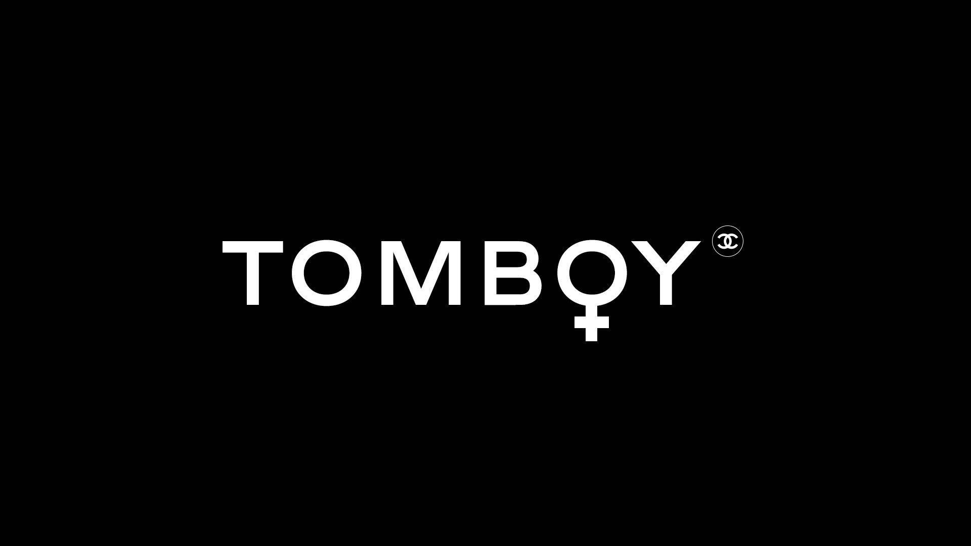 黑色 桌布 壁紙 — 粗體白色 'TOMBQY' 文字，帶有女性符號和 Chanel 標誌，居中在純黑色背景上。