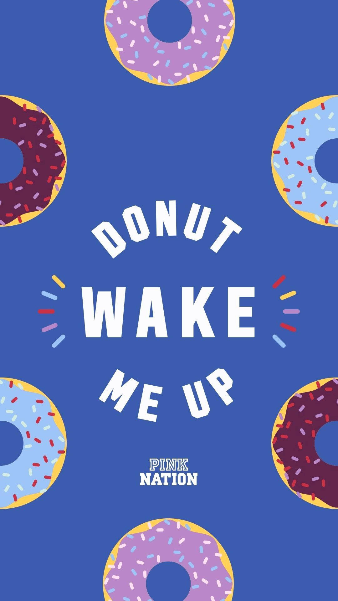 victoria 桌布 壁紙 — 粗體白色文字 'DONUT WAKE ME UP' 居中於藍色背景，周圍漂浮著色彩繽紛的糖霜甜甜圈。