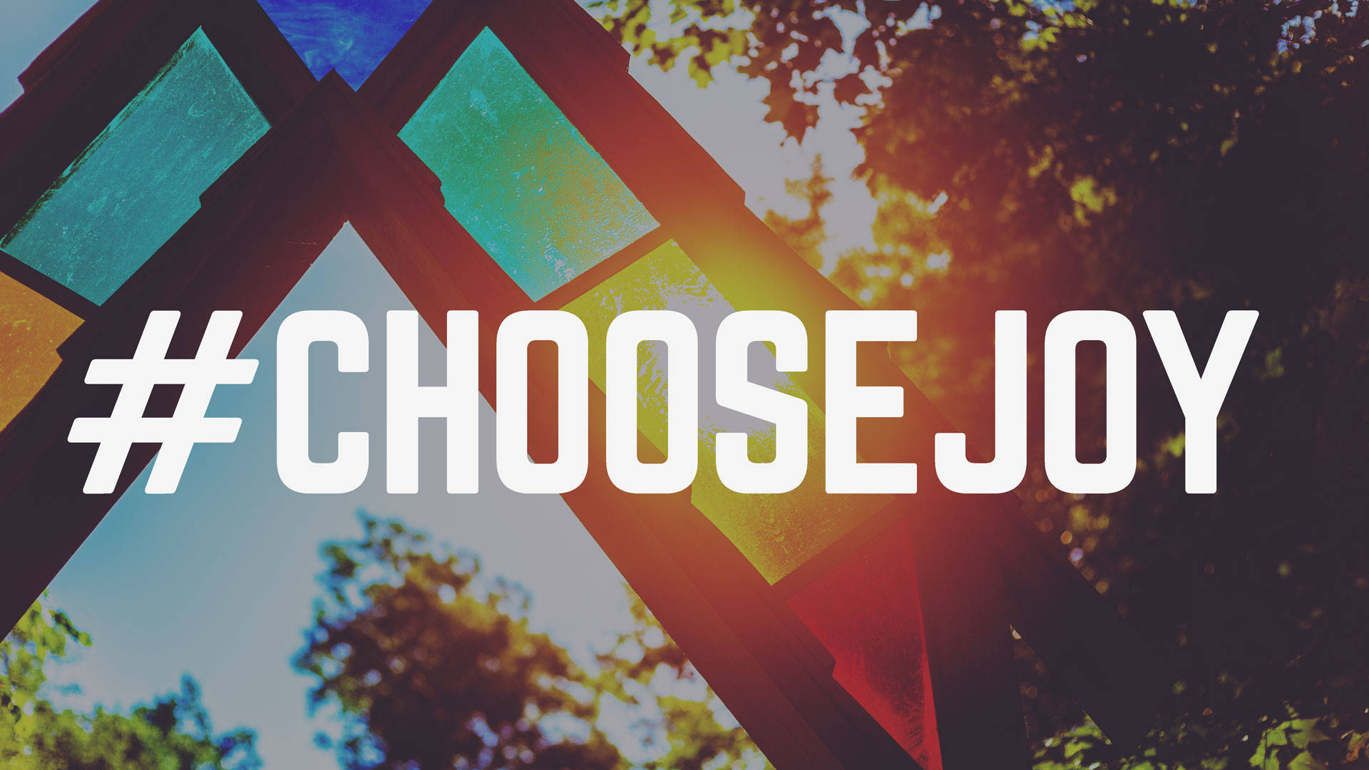 喜悅 桌布 壁紙 — 粗體白色文字 hashtag choosejoy 覆蓋在充滿活力的彩繪玻璃結構上，背景有陽光照射的樹木。