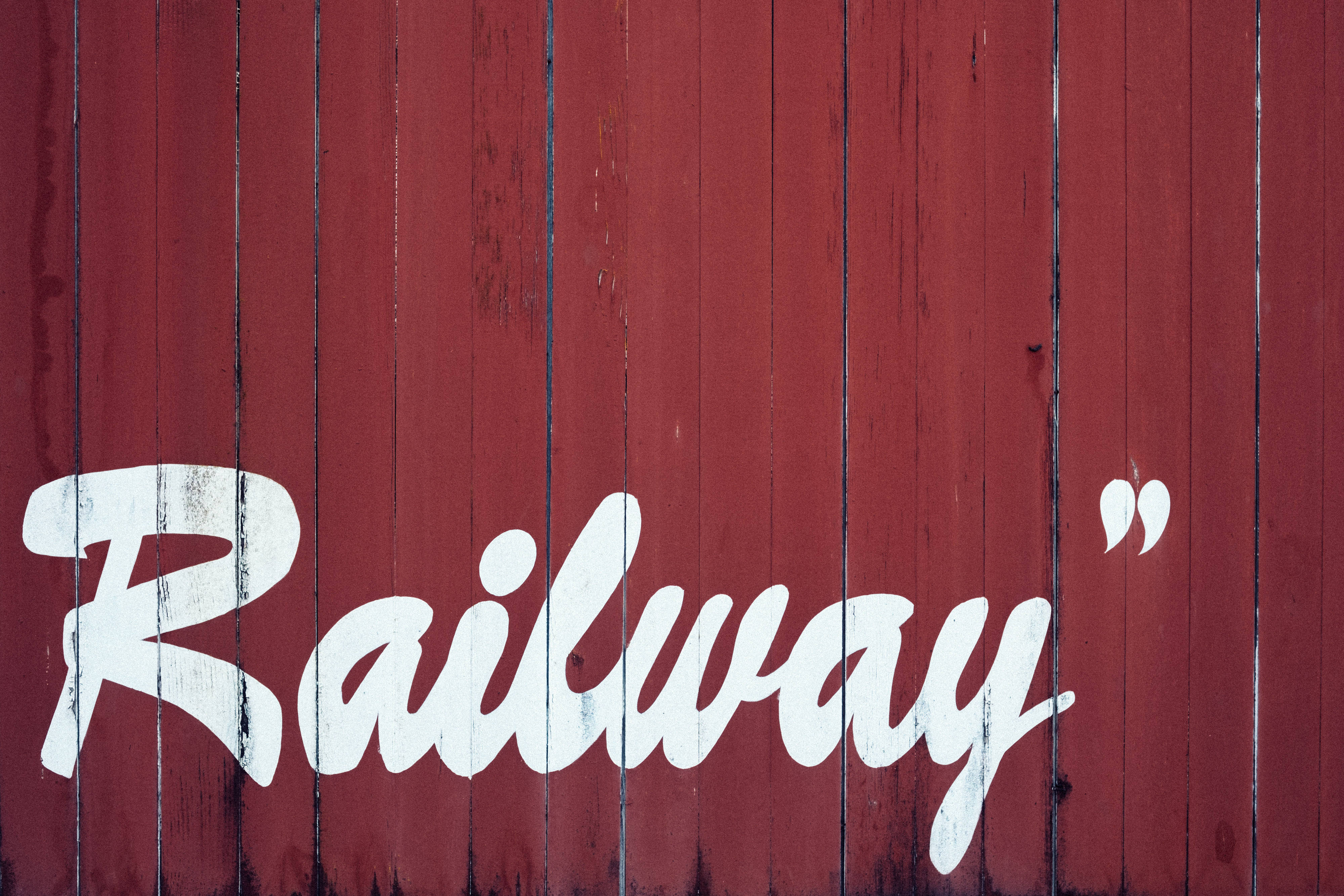 Red And White 桌布 壁紙 — 粗體白色草書 'Railway' 文字繪製在風化的紅色木板上，木紋清晰可見，油漆剝落。