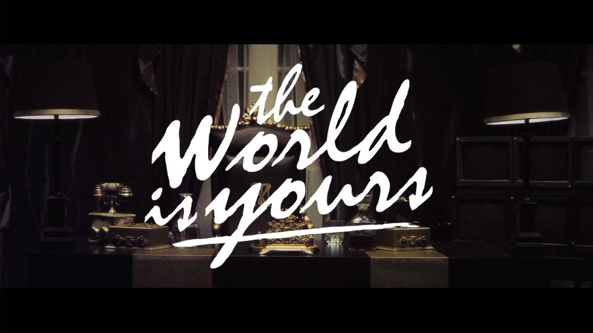 Desk 桌布 壁紙 — 粗體白色草書文字「The World is Yours」在燈光昏暗的復古房間中，與燈具和華麗裝飾一同閃耀。