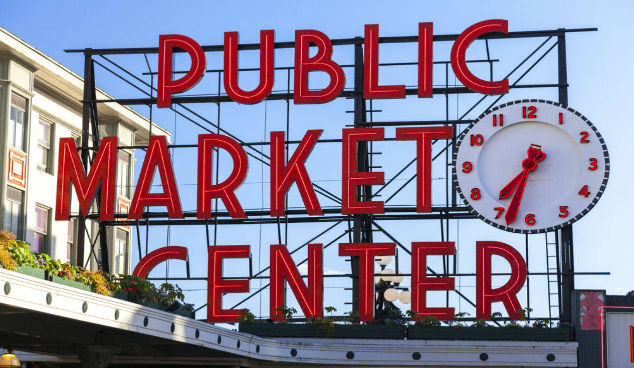 Pike Place Market 桌布 壁紙 — 粗體紅色字母拼出 PUBLIC MARKET CENTER，在晴朗的藍天下，一個大時鐘顯示 7:35。