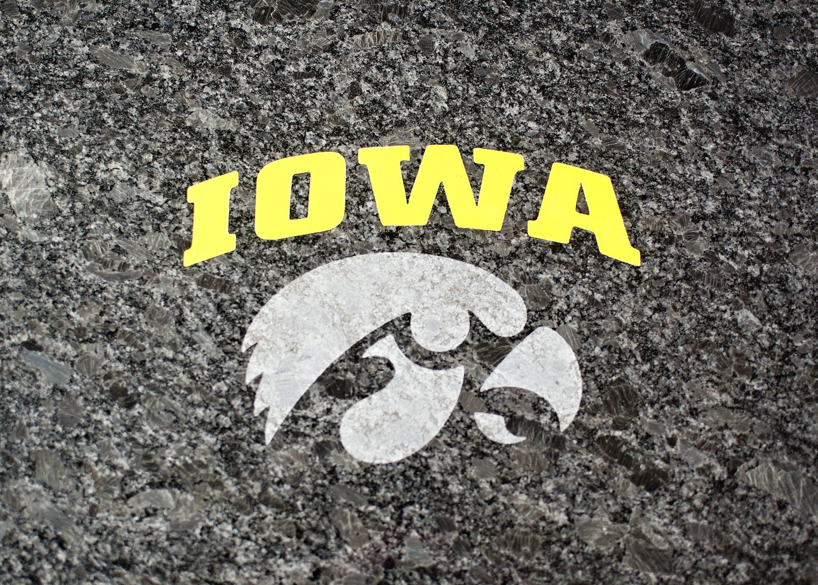 Iowa 桌布 壁紙 — 粗體黃色 IOWA 文字和白色鷹標誌蝕刻在深色斑點花崗岩表面上。