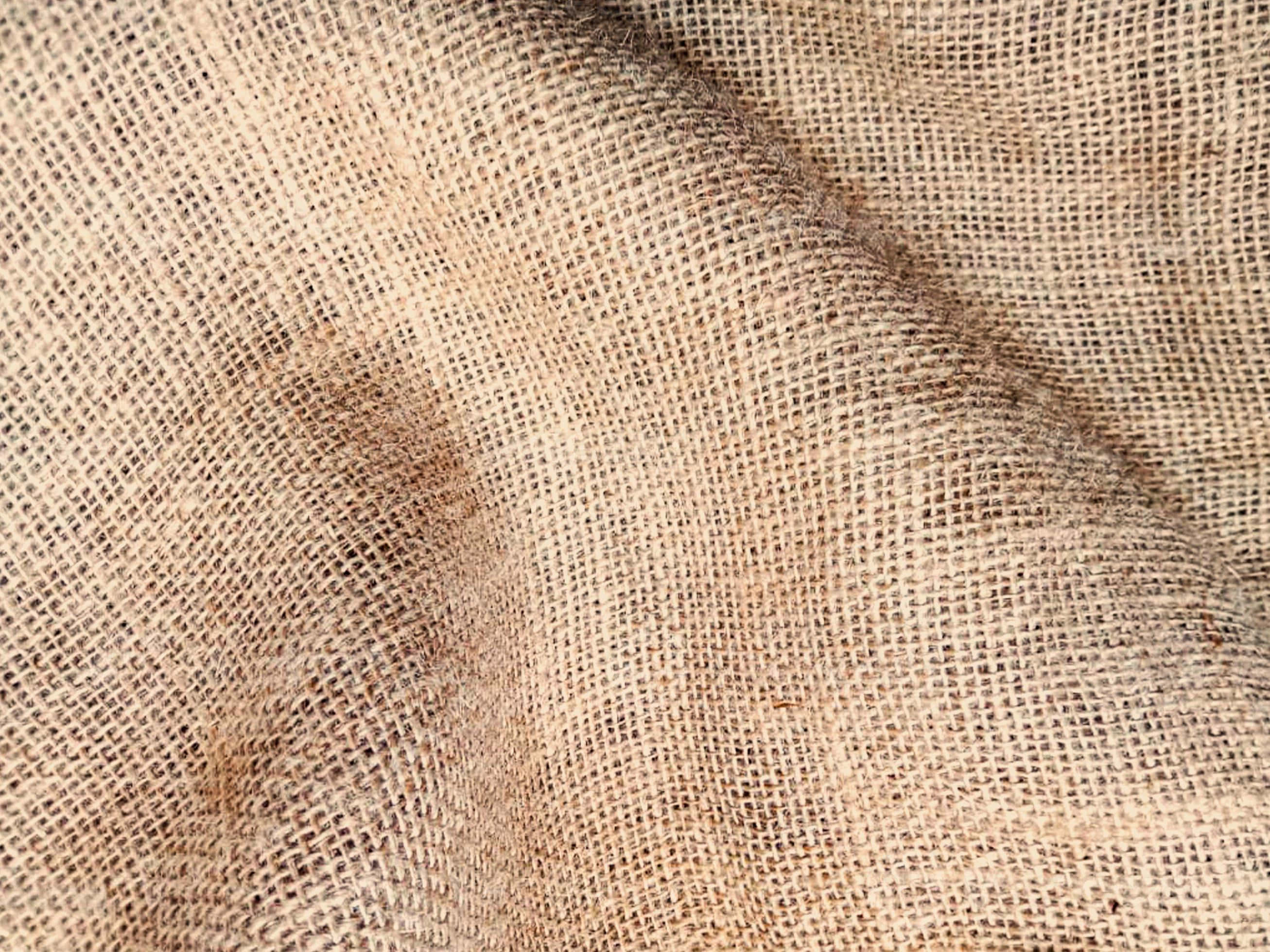 Burlap 桌布 壁紙 — 粗麻布料的特寫，帶有自然米色調和輕微污漬，顯示出有紋理的編織。