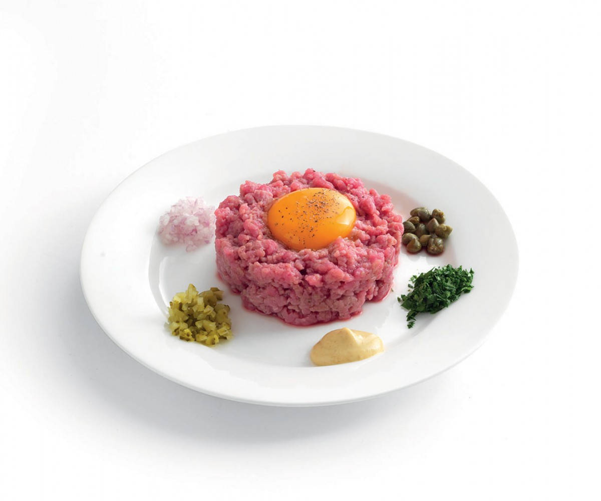 meat 桌布 壁紙 — 精心擺盤的牛肉塔塔，中央放有生蛋黃，並以酸豆、醃黃瓜、歐芹和洋蔥點綴在白色盤子上。