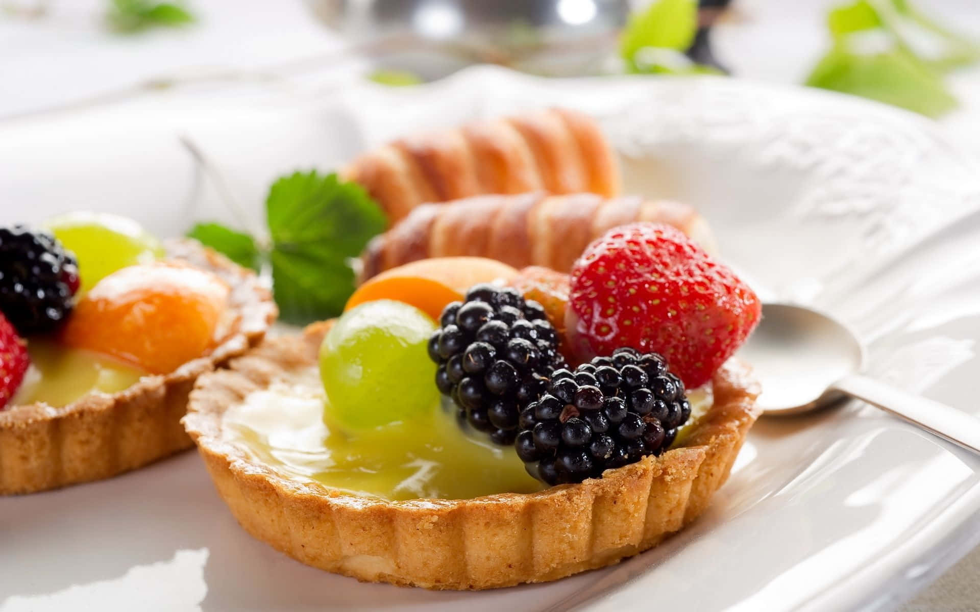 甜點 桌布 壁紙 — 精緻的水果塔，上面鋪滿鮮豔的草莓、黑莓和葡萄，在柔和光線下於白色盤子上閃閃發光。