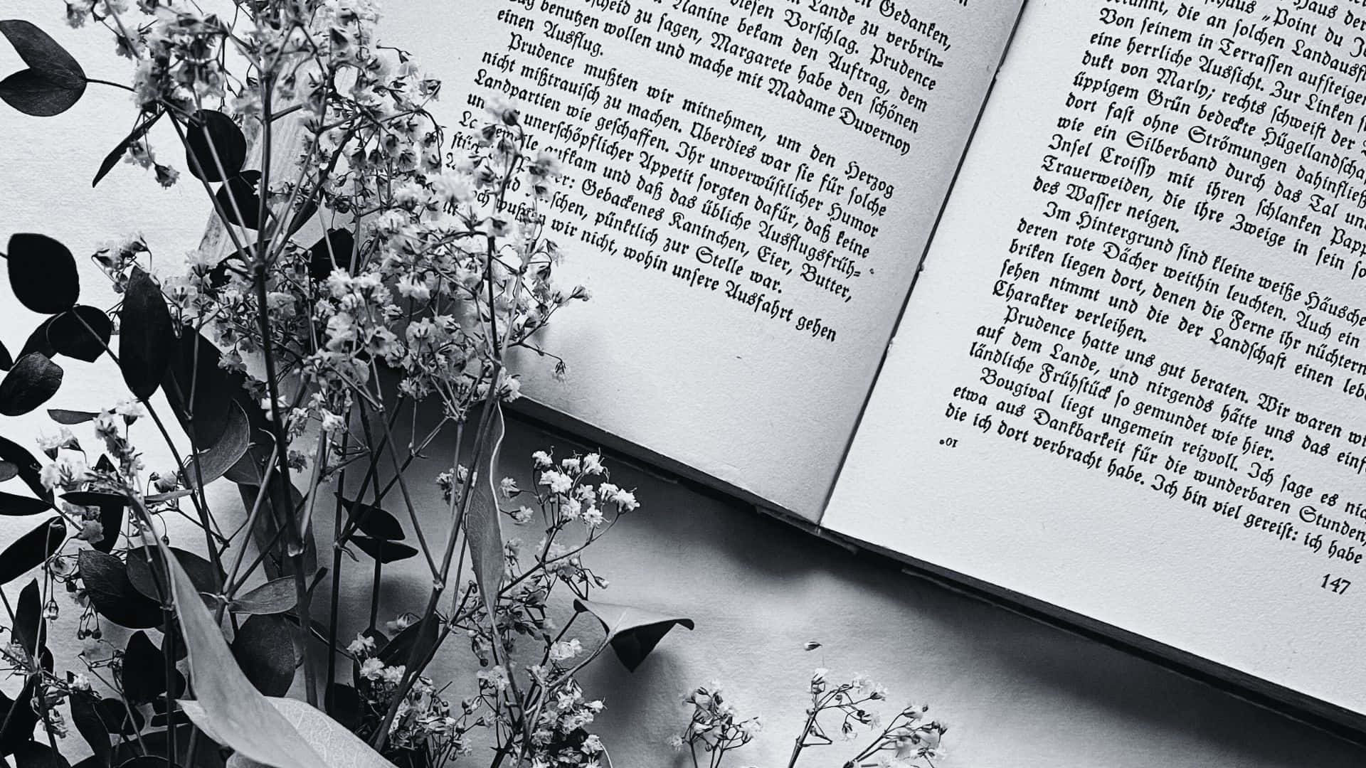 Black And White Book 桌布 壁紙 — 精緻的滿天星花朵放在一本打開的德文書上，構成單色調畫面。