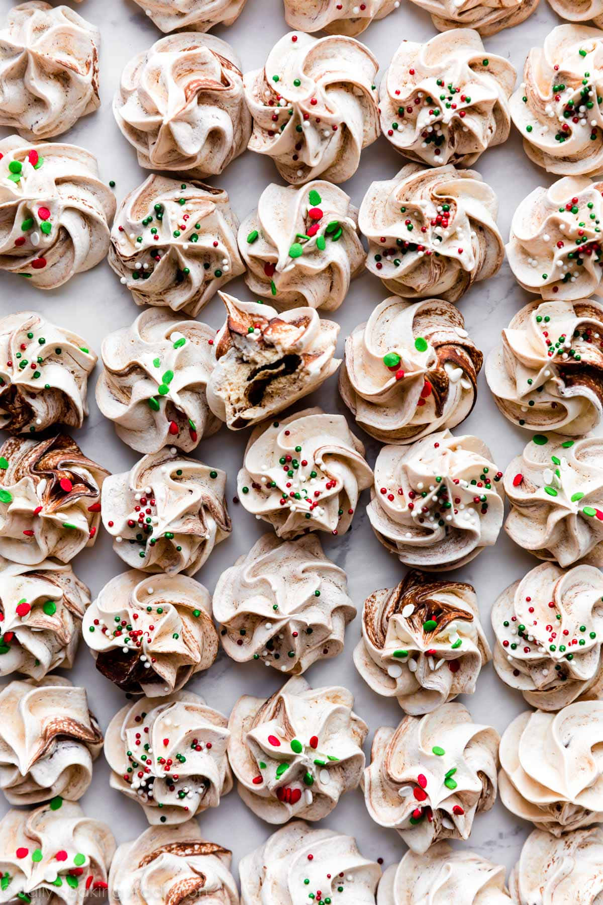 Meringue 桌布 壁紙 — 精緻的漩渦蛋白霜，飾有節慶紅綠糖粒和巧克力漩渦，整齊排列在大理石表面上。