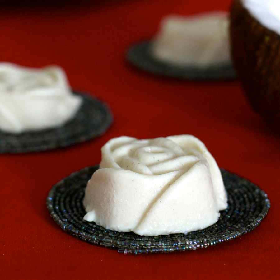 Blancmange 桌布 壁紙 — 精緻的白色玫瑰形狀甜點放在珠飾杯墊上，襯托著濃郁的紅色背景。
