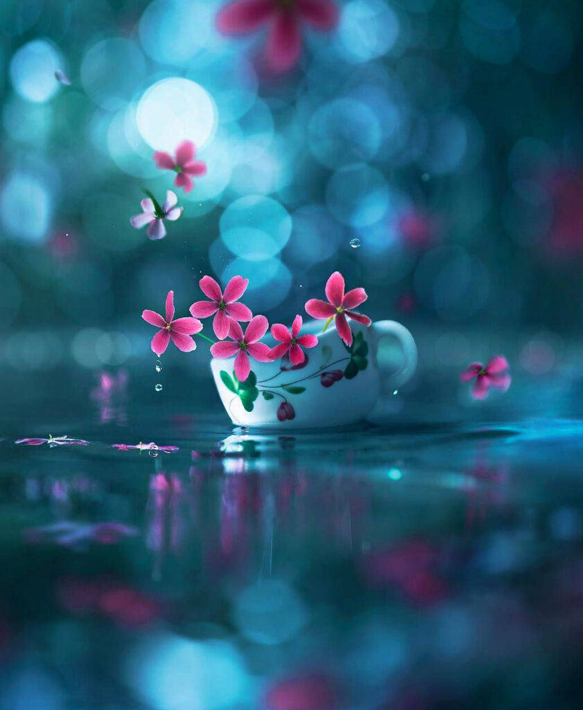 Chat 桌布 壁紙 — 精緻的白色茶杯漂浮在水面上，粉紅色的花朵從中綻放，背景是夢幻般的藍色散景。