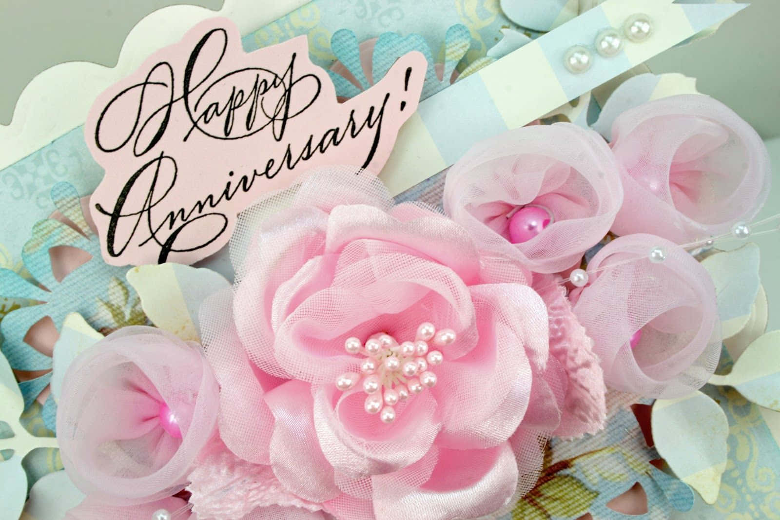 Anniversary 桌布 壁紙 — 精緻的粉紅色布料花藝佈置，帶有珍珠裝飾，並在圖案背景上放置「Happy Anniversary!」標誌。