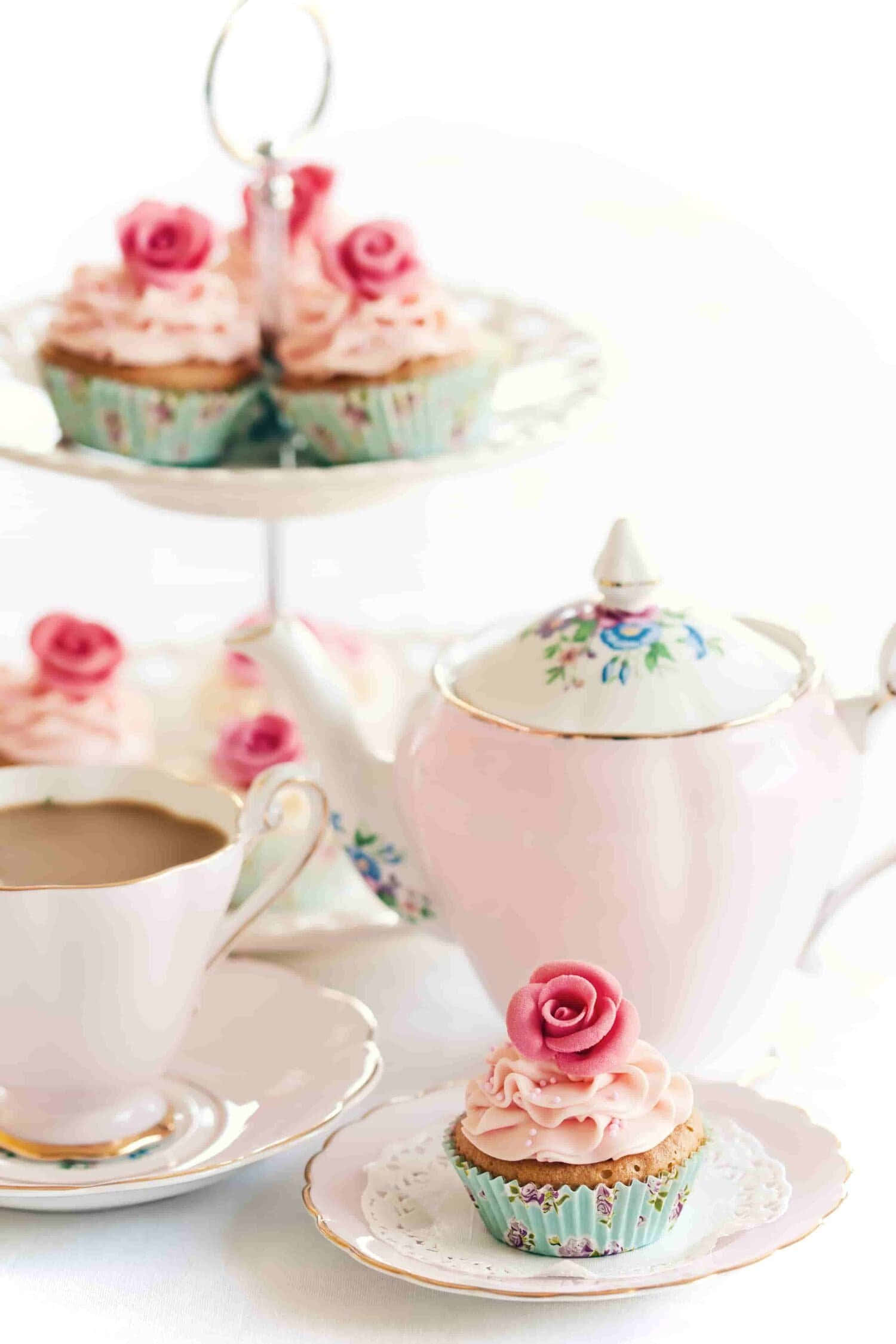 Tea Party 桌布 壁紙 — 精緻的粉紅色杯子蛋糕，上面有玫瑰糖霜，旁邊放著相配的茶壺和茶杯，在明亮的白色表面上。
