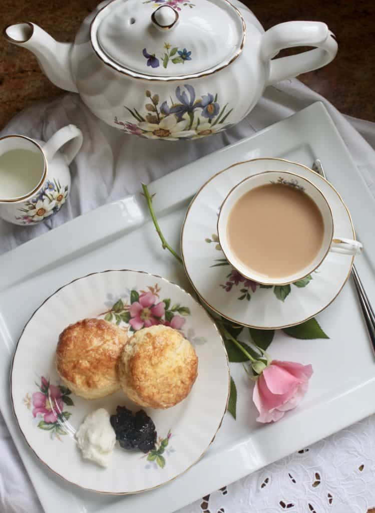 Teatime 桌布 壁紙 — 精緻的花卉茶壺和茶杯在白色托盤上，旁邊有一朵粉紅玫瑰，供應奶油茶配金黃司康、凝脂奶油和果醬。