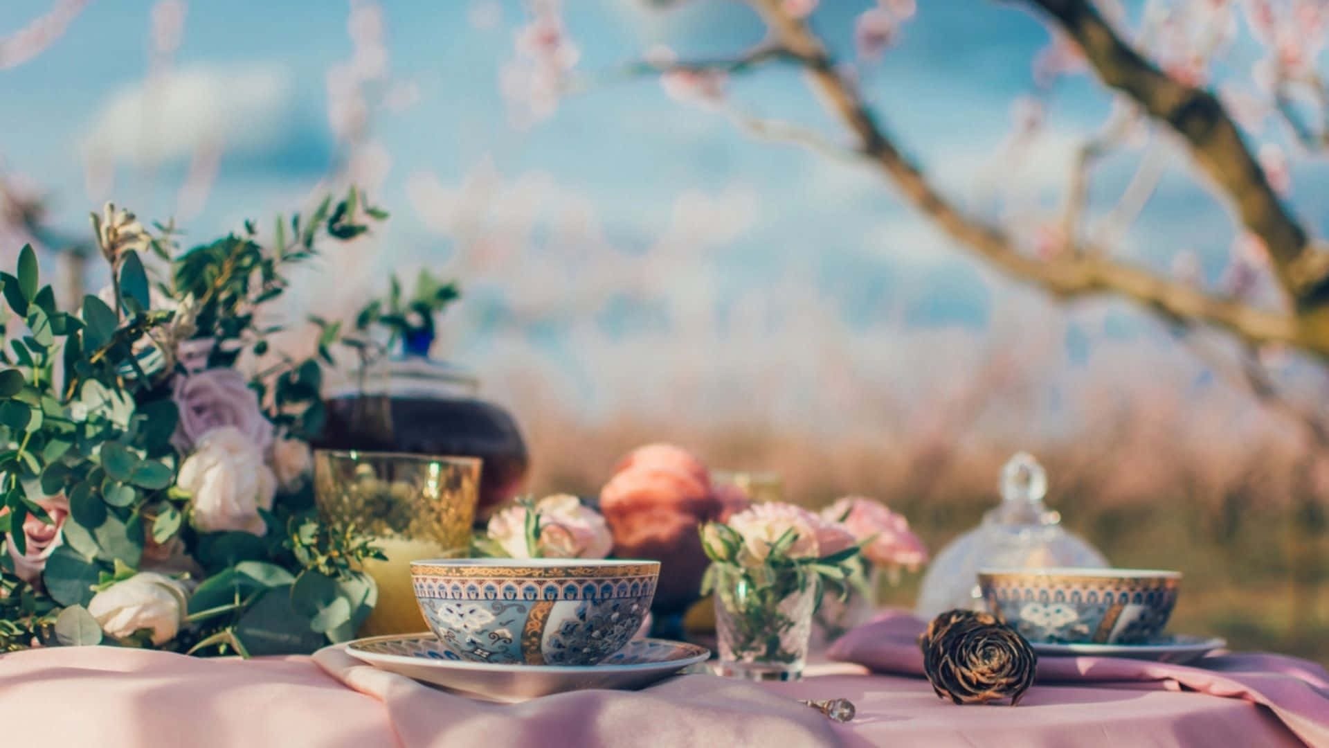 Tea Party 桌布 壁紙 — 精緻的茶具放在粉紅色的布上，襯托著盛開的櫻花和柔和的藍天。