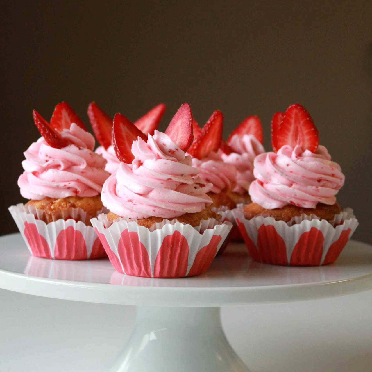 Pink Cupcakes 桌布 壁紙 — 精緻的草莓杯子蛋糕，配上粉紅色糖霜和新鮮草莓片，優雅地擺放在白色蛋糕架上。