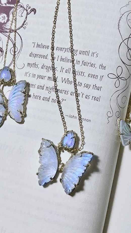 Butterfly Jewelry 桌布 壁紙 — 精緻的藍色蝴蝶項鍊放在一本打開的書頁上，書頁上有奇幻的文字和華麗的邊框。