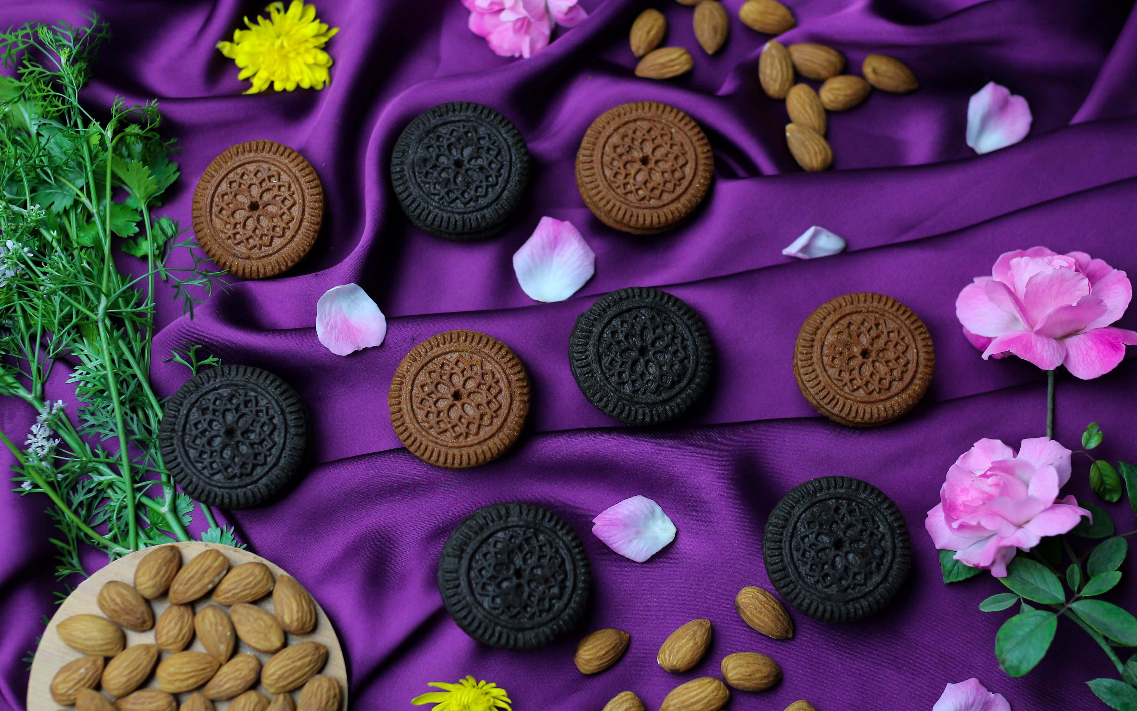 Cookies 桌布 壁紙 — 精緻的餅乾、杏仁和花朵藝術地排列在豐富的紫色緞面布料上，營造出奢華的靜物構圖。