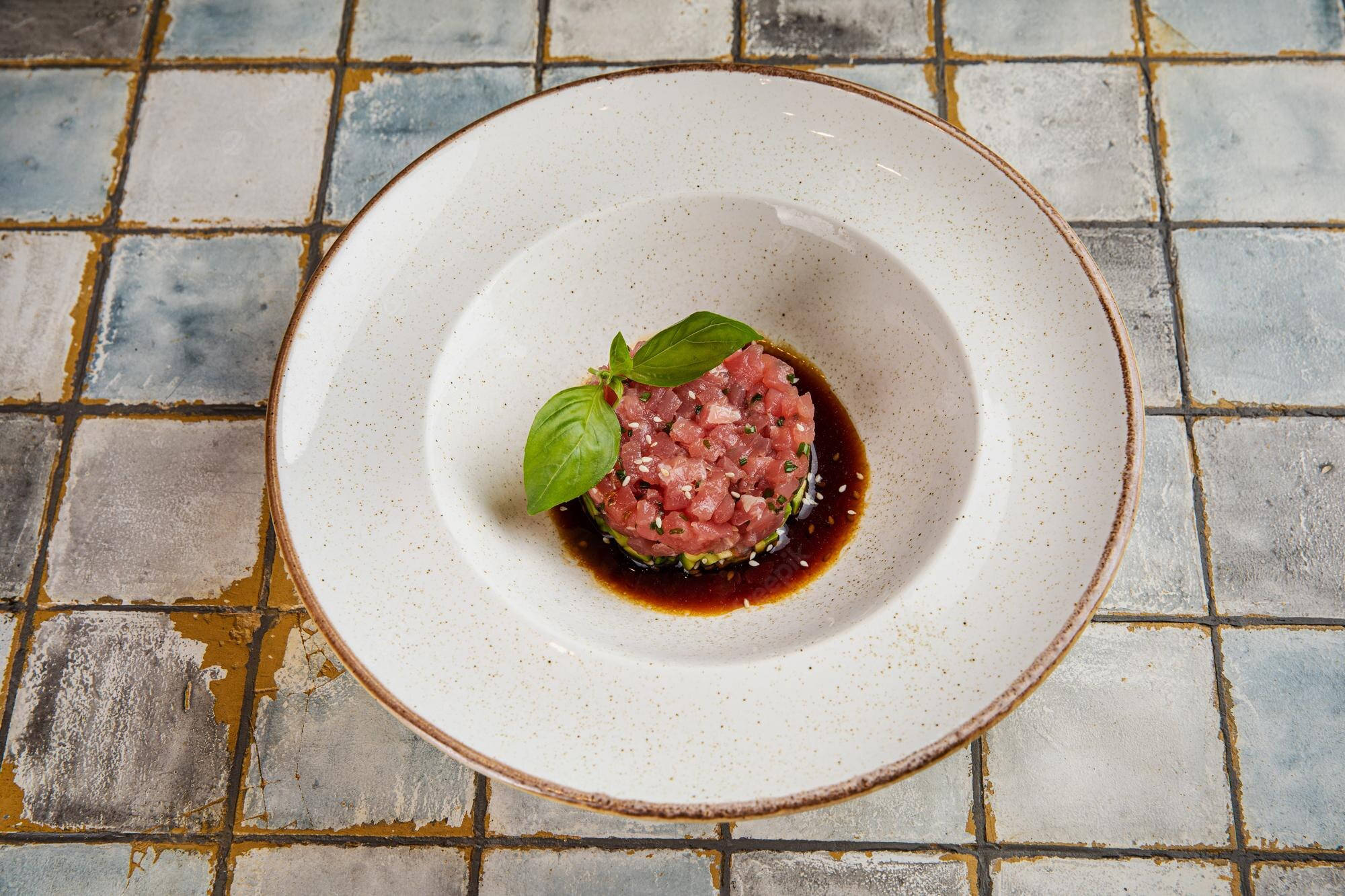 meat 桌布 壁紙 — 精緻的鮪魚他他，飾以羅勒和芝麻，盛載於斑點白碗中，置於風化瓷磚表面上。