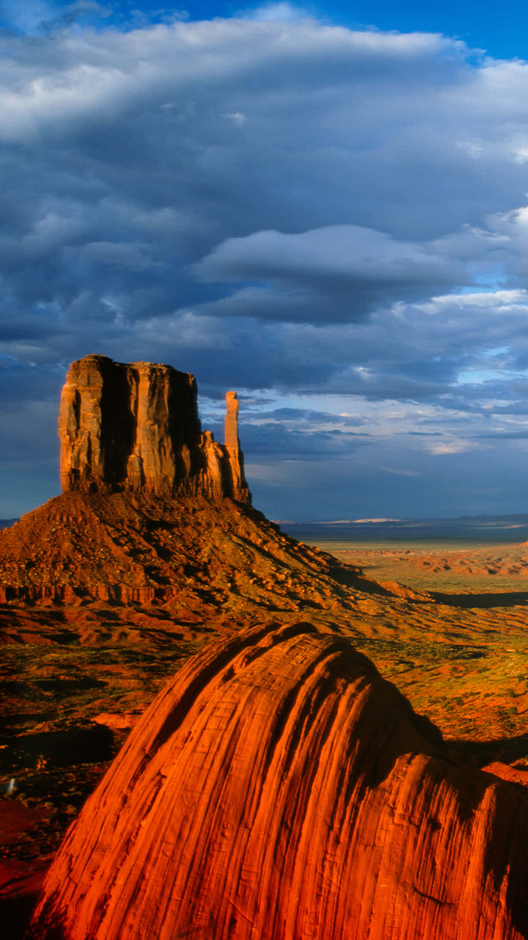 Arizona 桌布 壁紙 — 紀念碑谷的標誌性孤峰在日落時分，在戲劇性的多雲天空映襯下，散發著溫暖的橙色光芒。