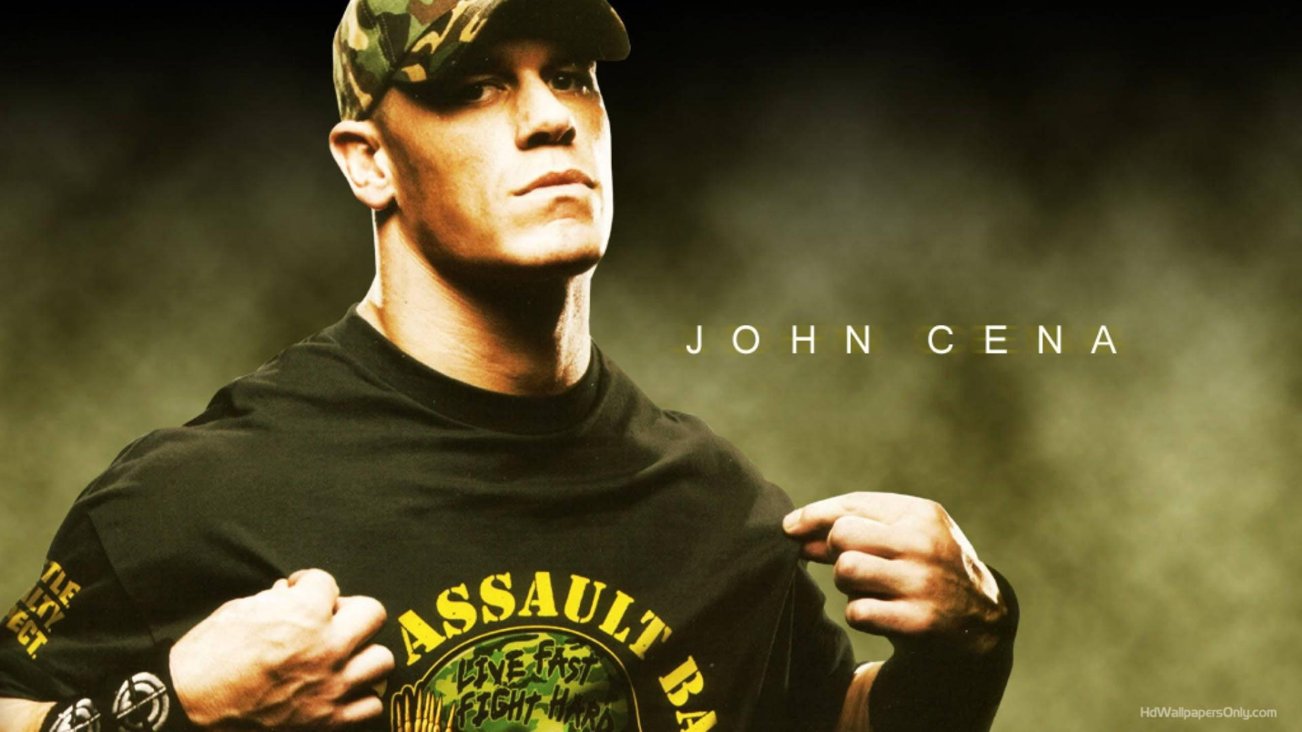 約翰·希南 桌布 壁紙 — 約翰·希南（John Cena）用力拉扯他的黑色T恤，露出大膽的黃色圖案，背景是煙霧繚繞的綠色，眼神專注。