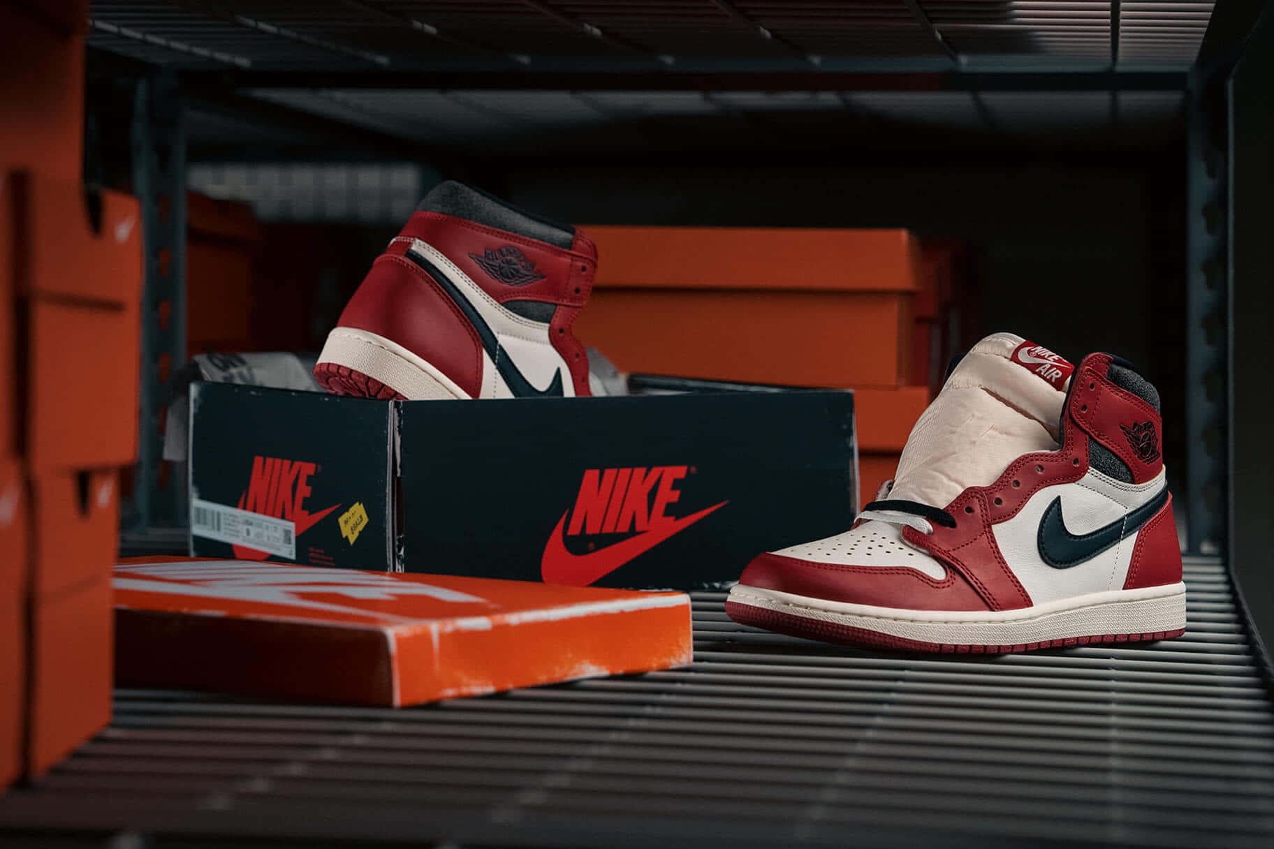 鞋子 桌布 壁紙 — 紅、白、黑色Nike Air Jordan 1運動鞋陳列在金屬架上，旁邊有品牌鞋盒，倉庫燈光昏暗。