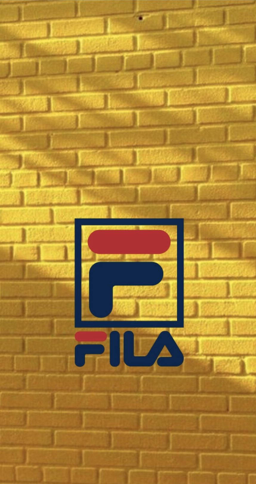 Fila 桌布 壁紙 — 紅、藍、白色的 Fila 標誌在紋理黃磚牆上格外醒目，斑駁的陽光投下陰影。