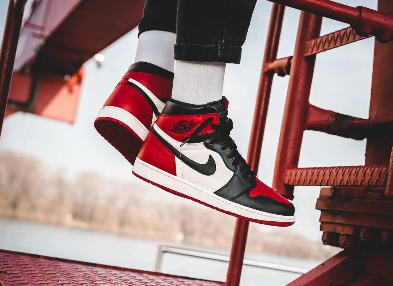 Air Jordan 1 桌布 壁紙 — 紅、黑、白色高筒運動鞋懸掛在生鏽的金屬樓梯半空中，背景是模糊的冬日景色。
