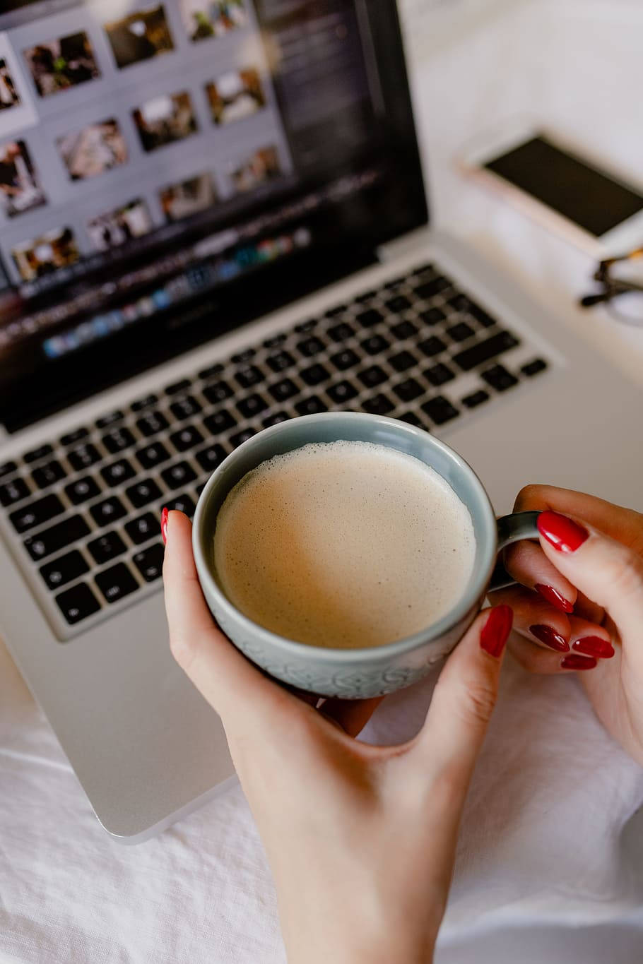 Best Laptop 桌布 壁紙 — 紅指甲的手在打開的筆記型電腦旁捧著冒煙的杯子，筆記型電腦顯示照片縮圖。