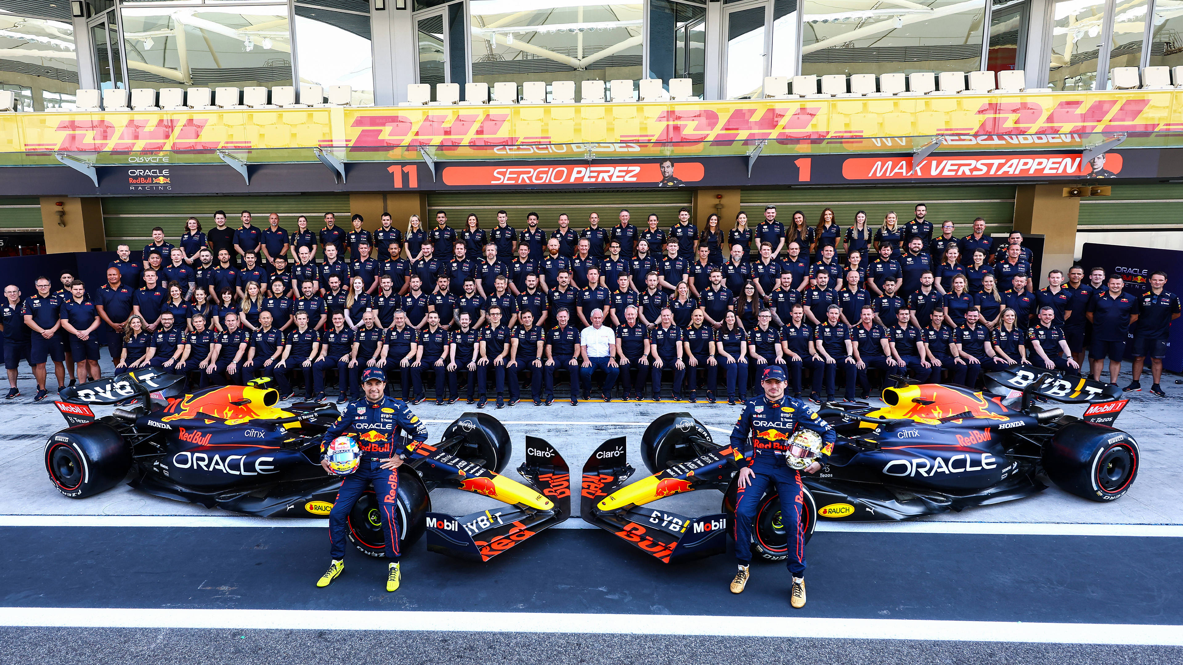 F1 桌布 壁紙 — 紅牛一級方程式車隊在維修站車庫前與兩輛賽車及穿著制服的工作人員合影。