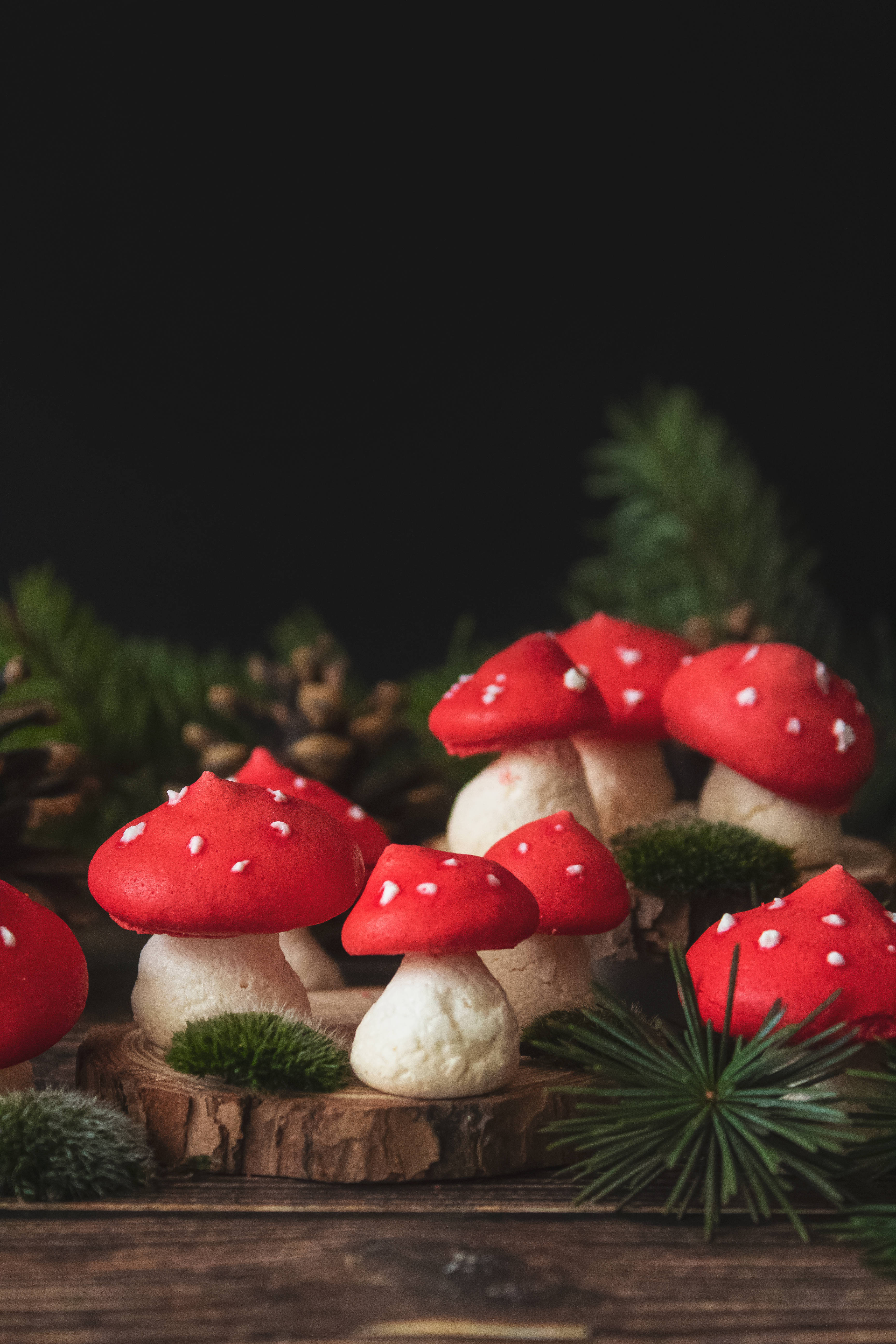 Cute Mushroom 桌布 壁紙 — 紅白波點蘑菇餅乾放在質樸的木片上，搭配松針和松果，背景為深色。
