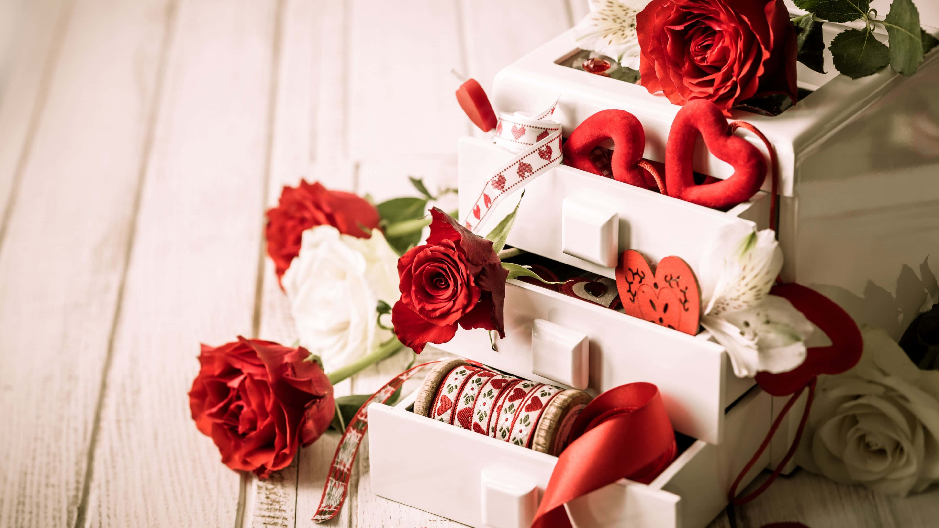 Red Roses 桌布 壁紙 — 紅白玫瑰從一個裝飾著心形、絲帶和節日裝飾的白色分層盒子中溢出，放在質樸的木質表面上。
