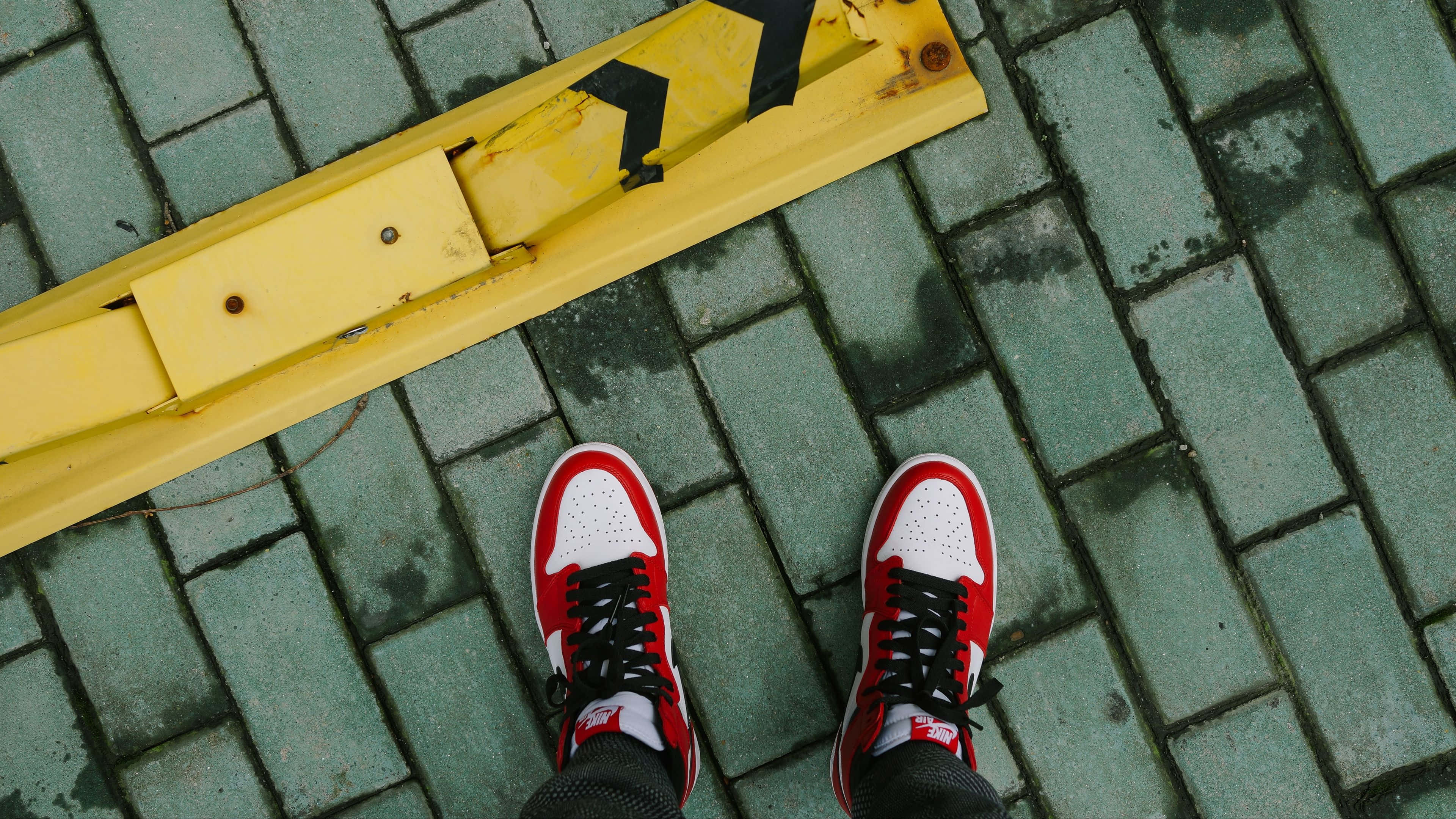 Sneaker 桌布 壁紙 — 紅白運動鞋站在潮濕的綠色磚塊上，旁邊是一條風化的黃色路緣石。
