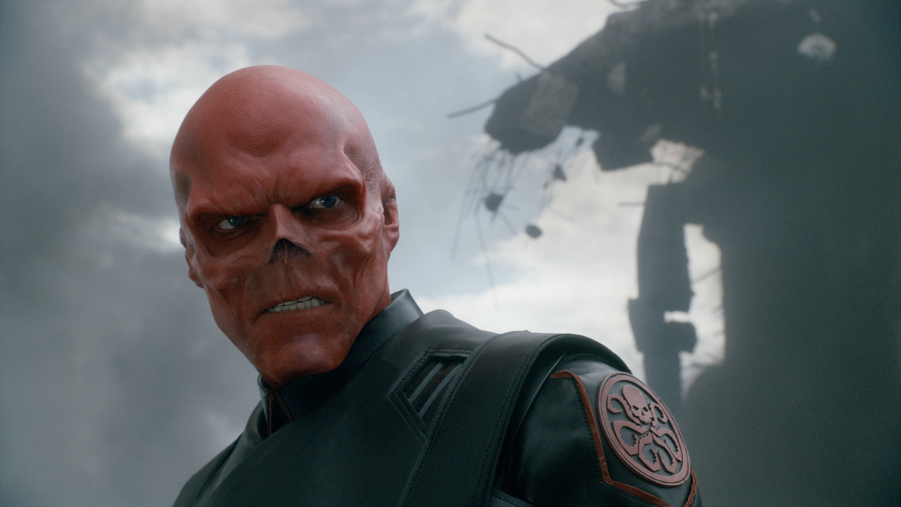 Red Skull 桌布 壁紙 — 紅皮膚、骷髏臉的惡棍，身穿黑色戰術裝備，在暴風雨的天空和破碎的建築物前凝視。